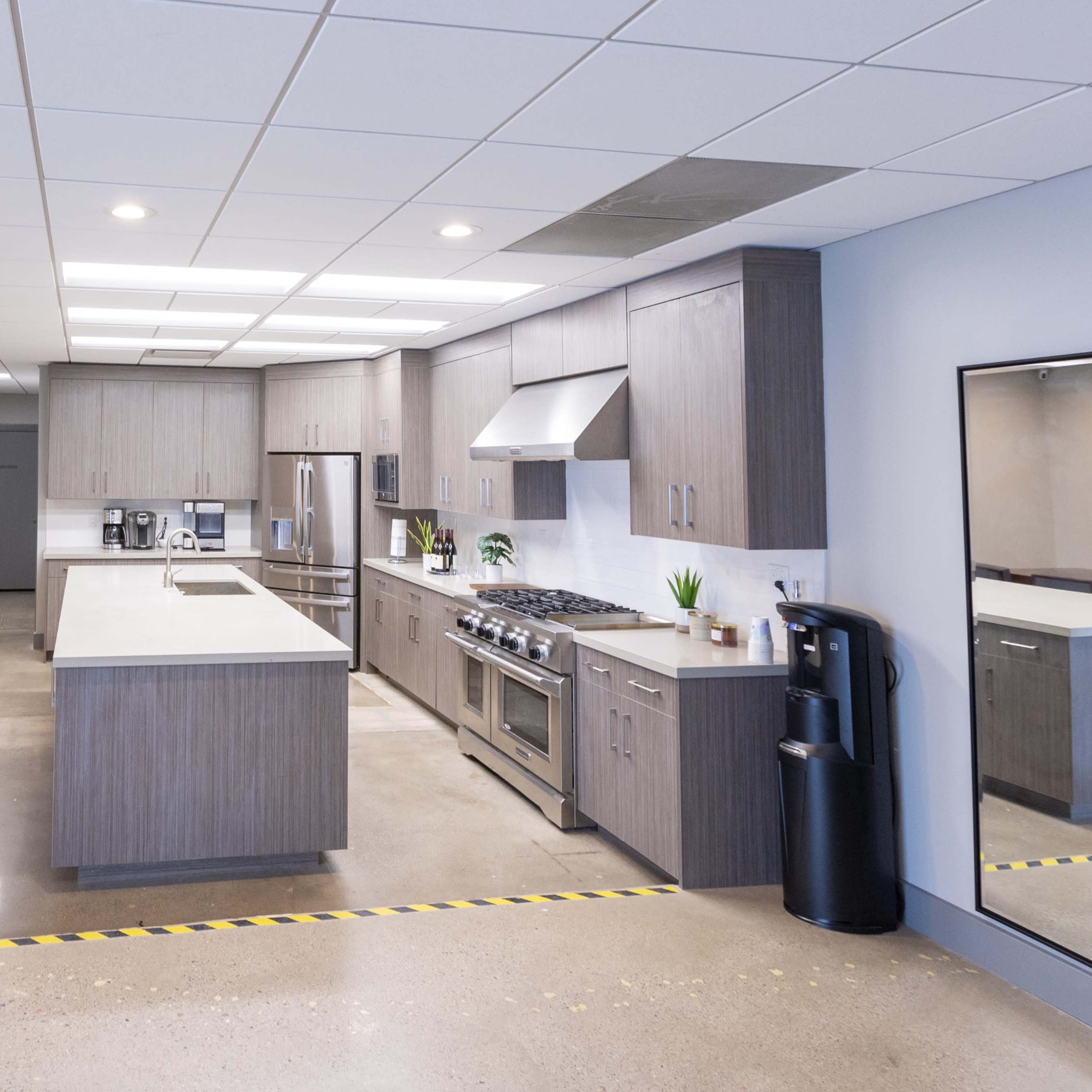 A modern kitchen area with gray cabinets, stainless steel appliances, a dining table, and a large mirror along the wall.