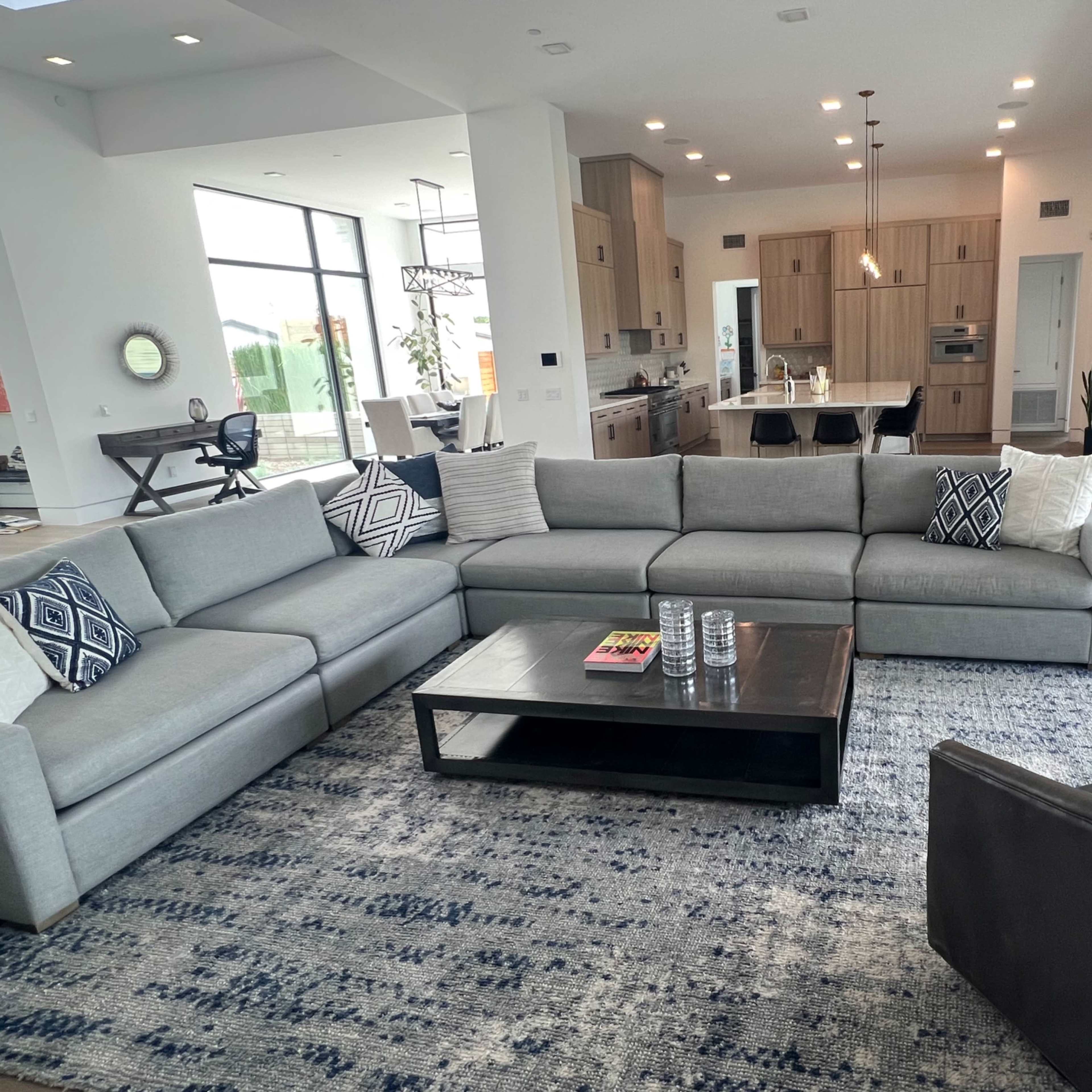 A modern living room with a sectional sofa, a coffee table, and a view of an open kitchen in the background.