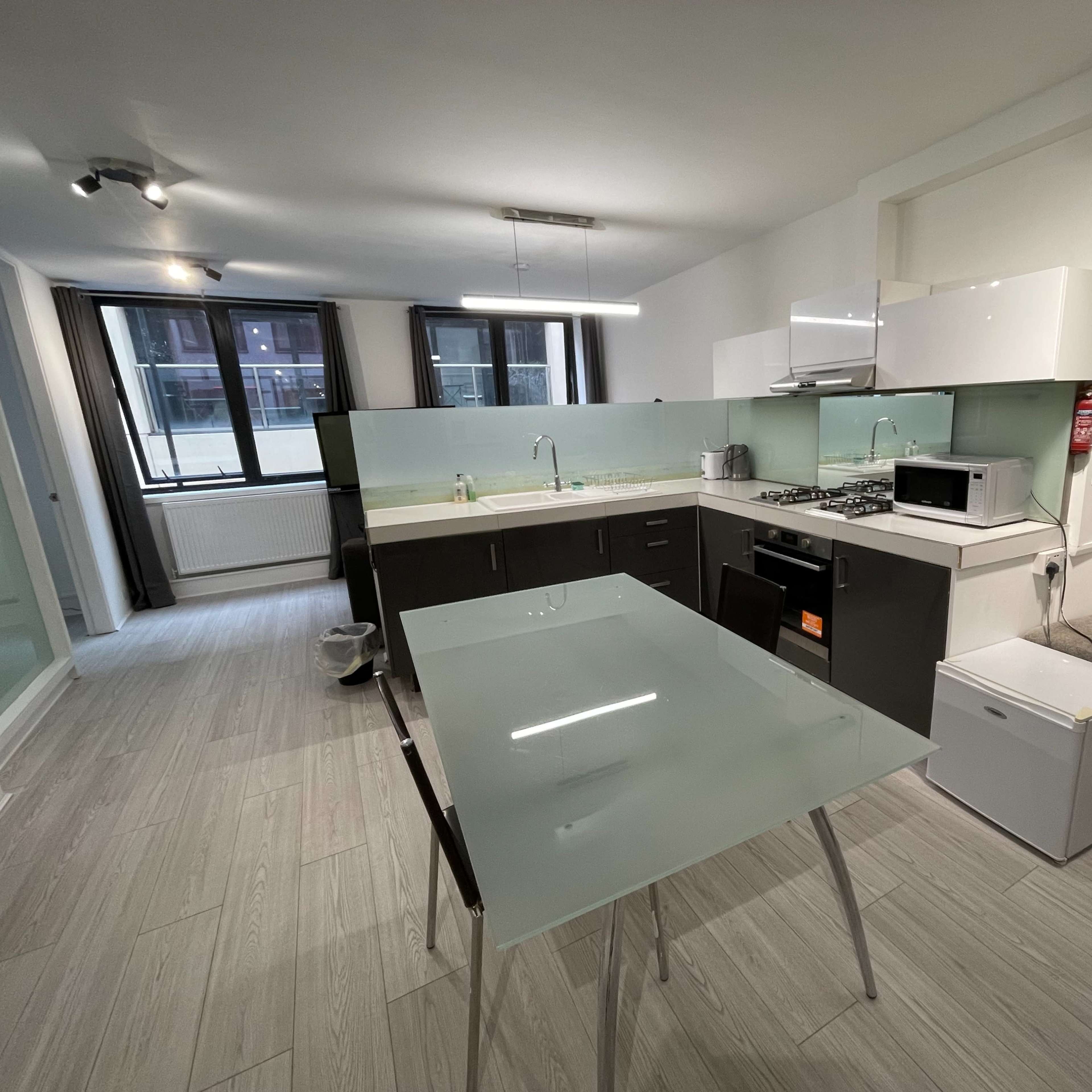 A modern kitchen with a glass dining table, a gas stove, a microwave, and large windows allowing natural light.