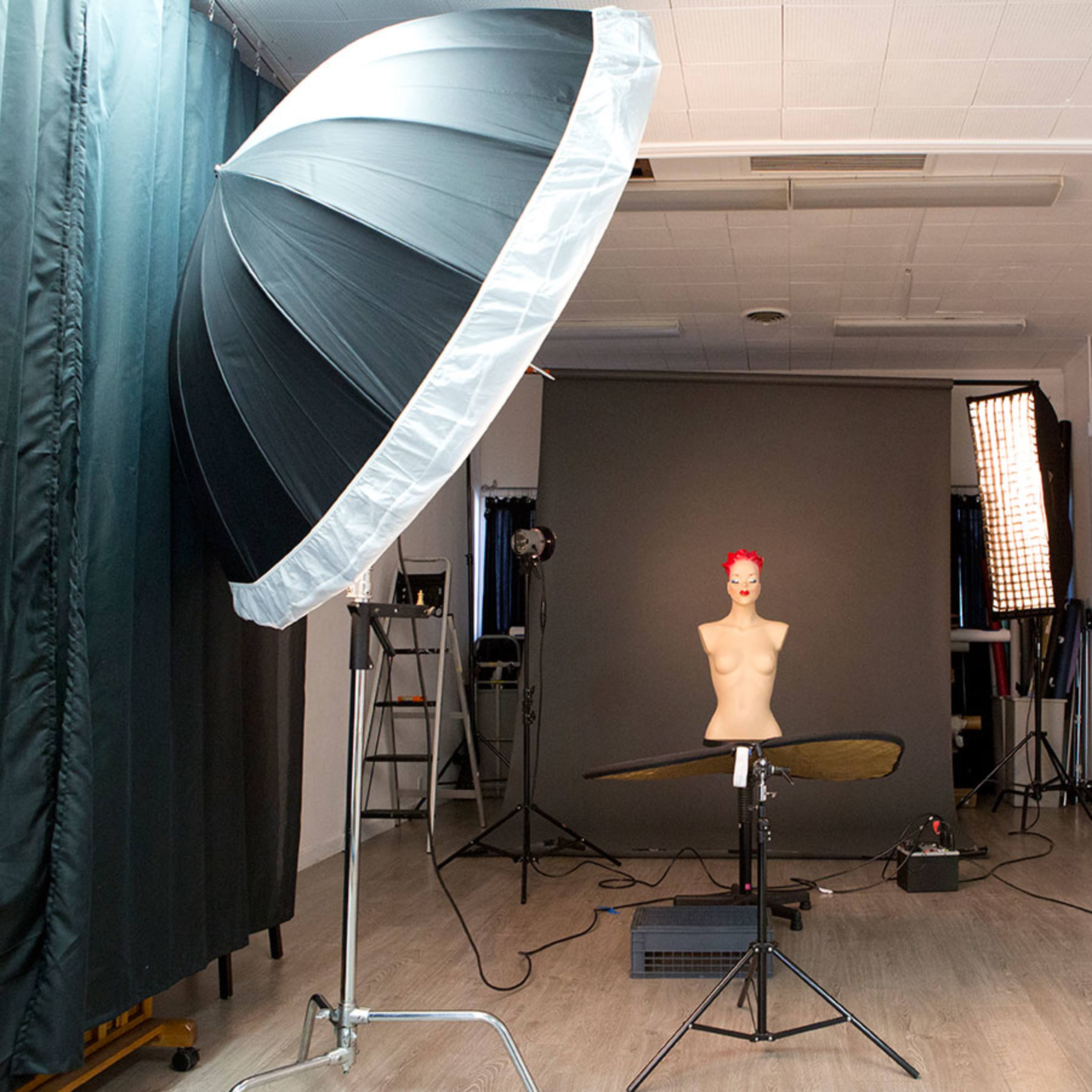 A photography studio is set up with a mannequin on a table, large softboxes for lighting, and a backdrop in the background.