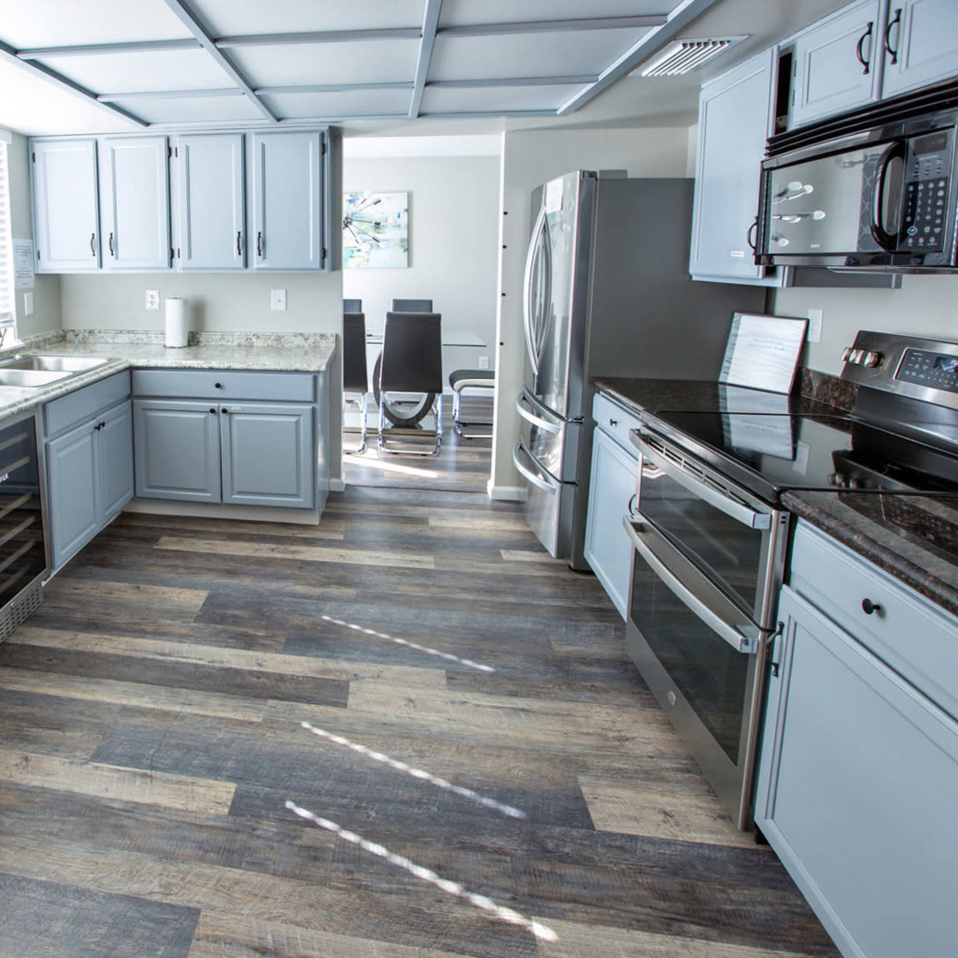 The kitchen features gray cabinets, a stainless steel refrigerator and oven, and a countertop made of granite, with a window allowing natural light to enter the space.
