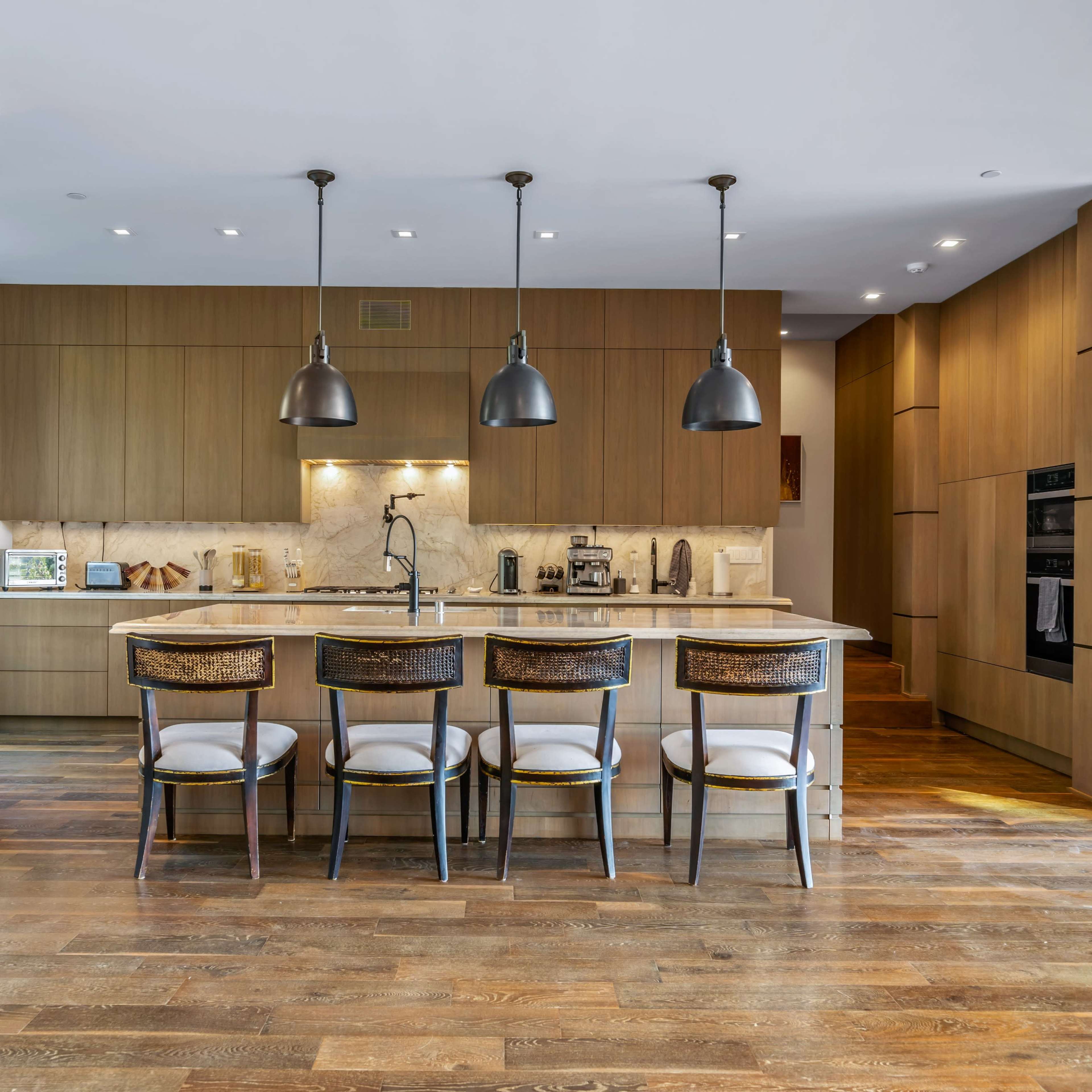 A modern kitchen with wooden cabinetry, a large island with bar seating, and pendant lighting above.