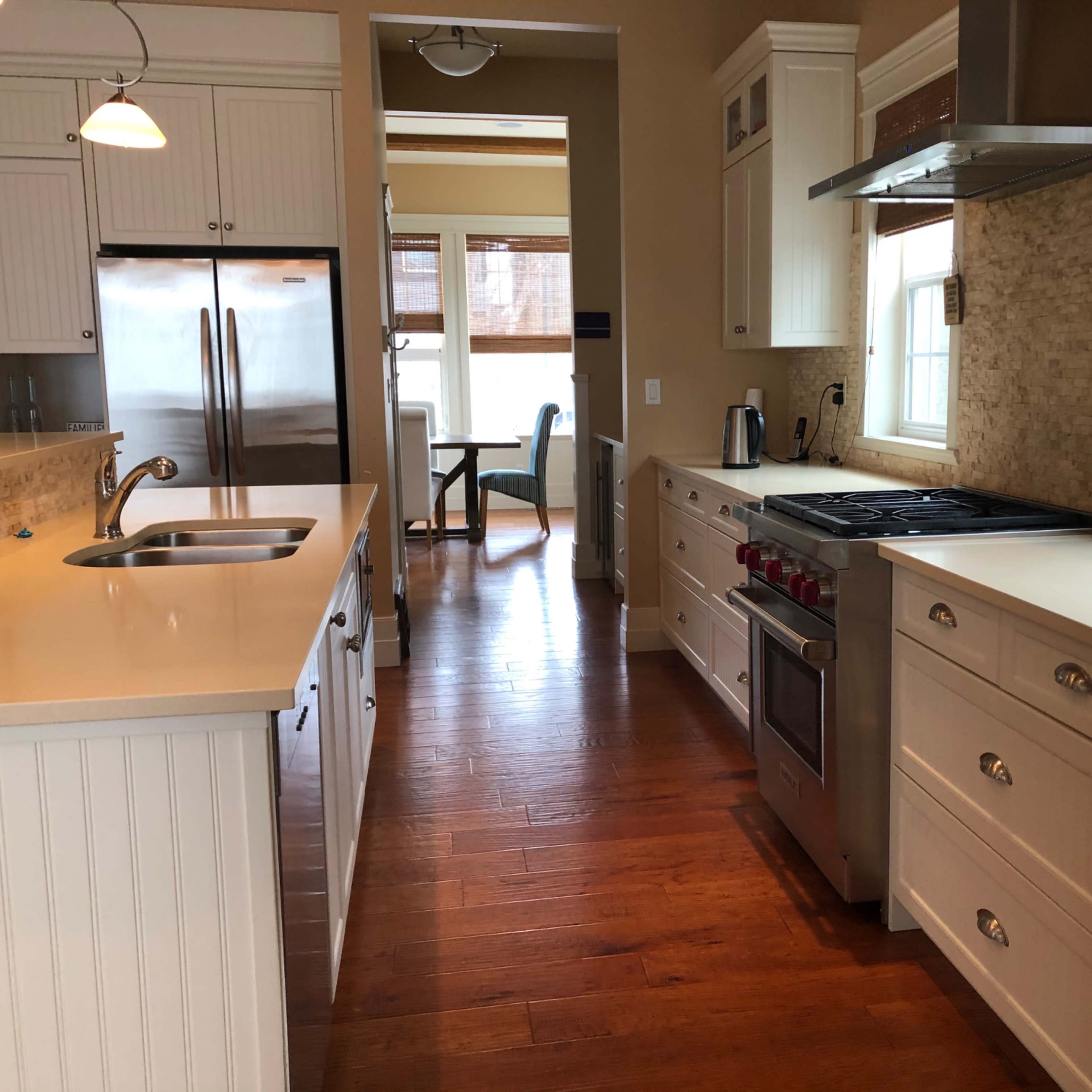 A modern kitchen featuring white cabinetry, stainless steel appliances, and hardwood flooring.
