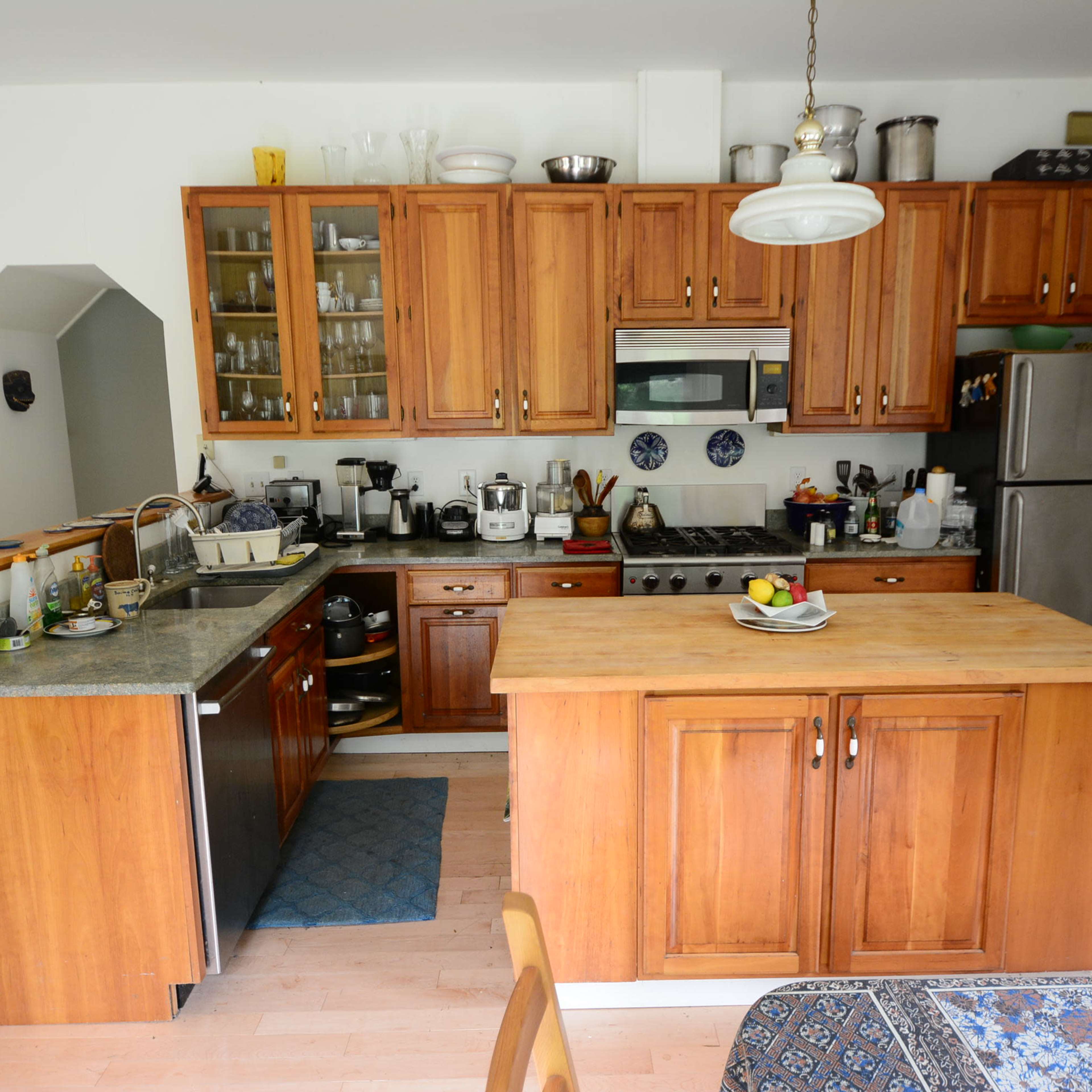 A kitchen with wooden cabinetry, a central island, stainless steel appliances, and a dining table set with a patterned tablecloth.
