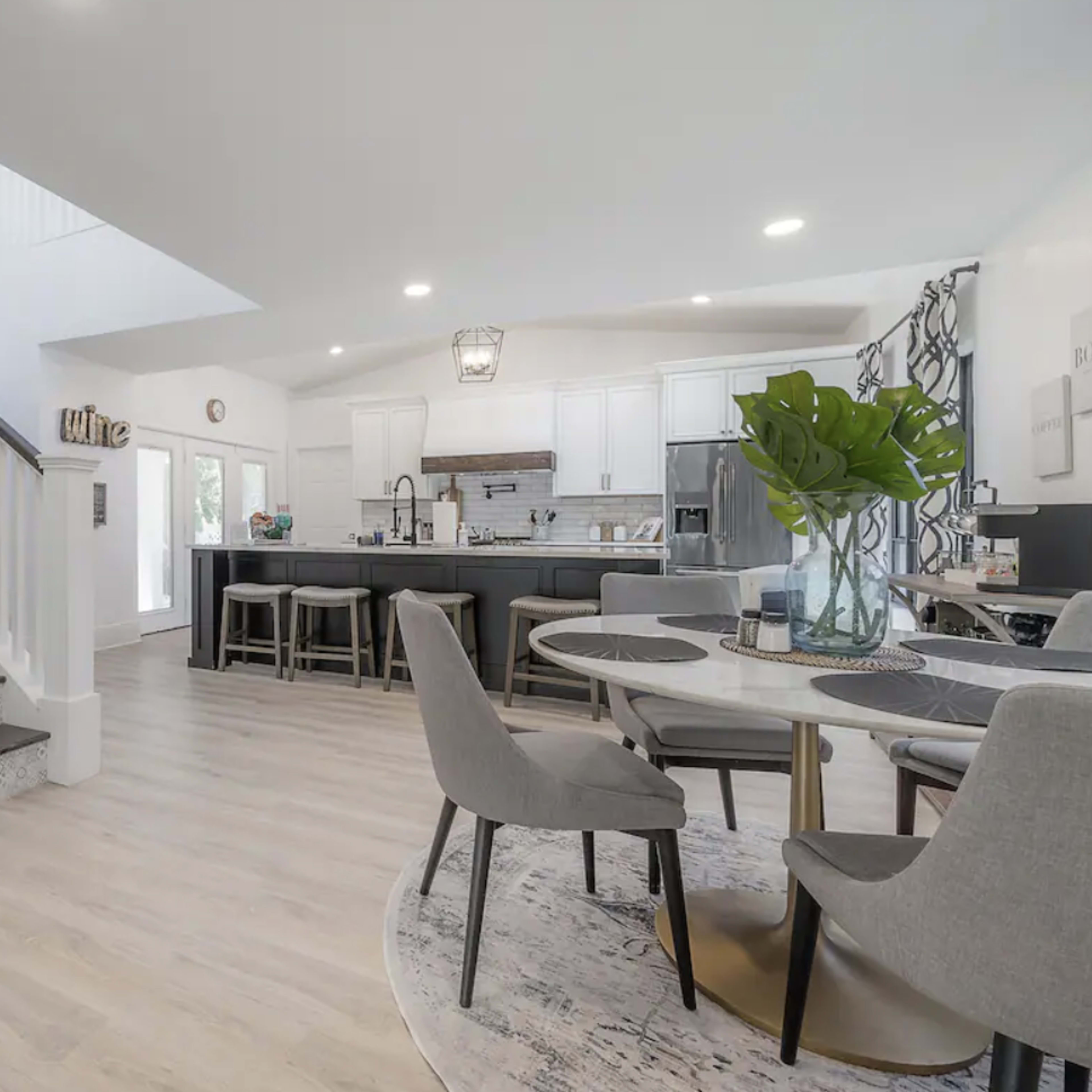 A spacious open-concept living area features a kitchen with dark cabinetry and a dining area with a circular table adjacent to a staircase.