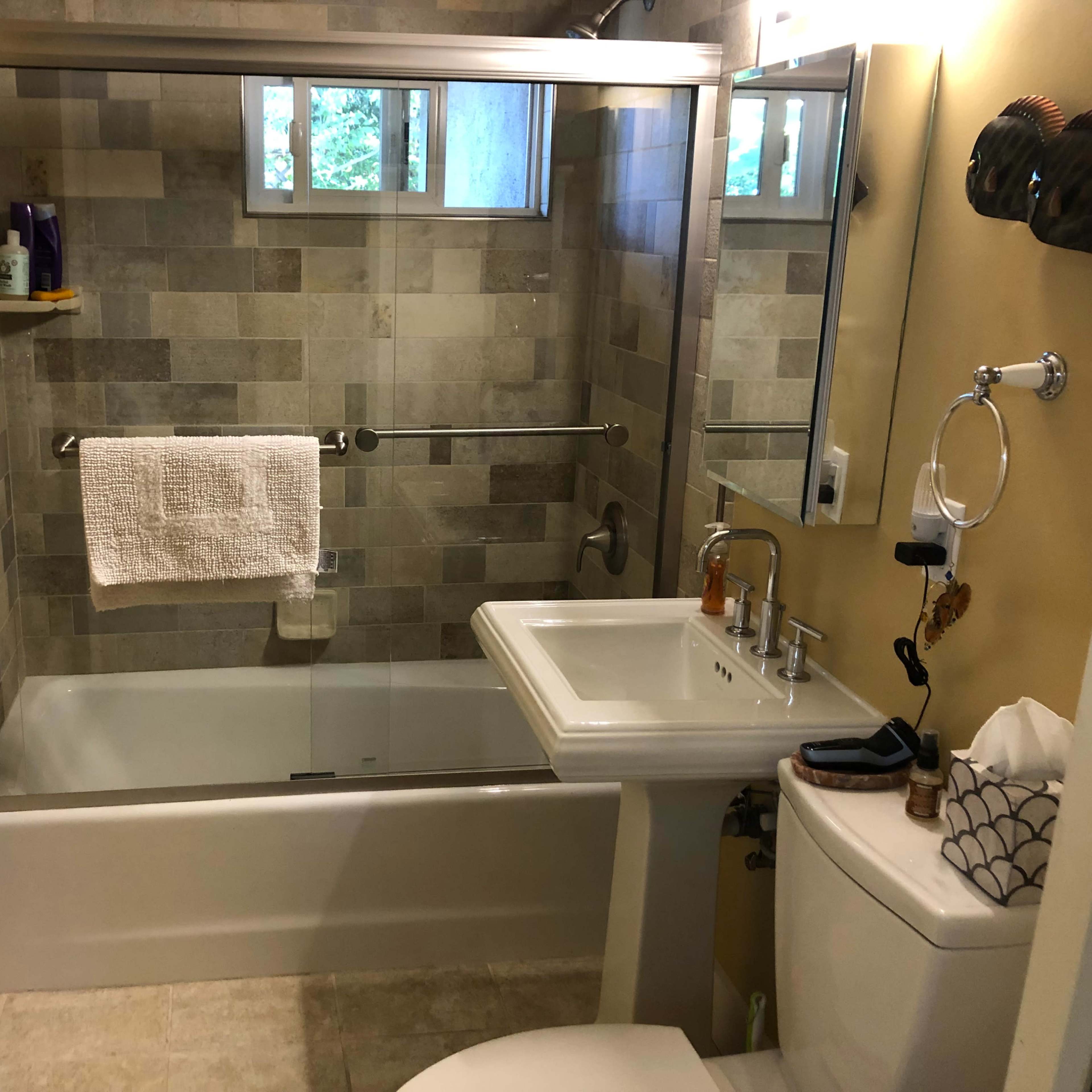 A bathroom with a tiled shower, bathtub, sink, toilet, and various toiletries displayed on shelves.