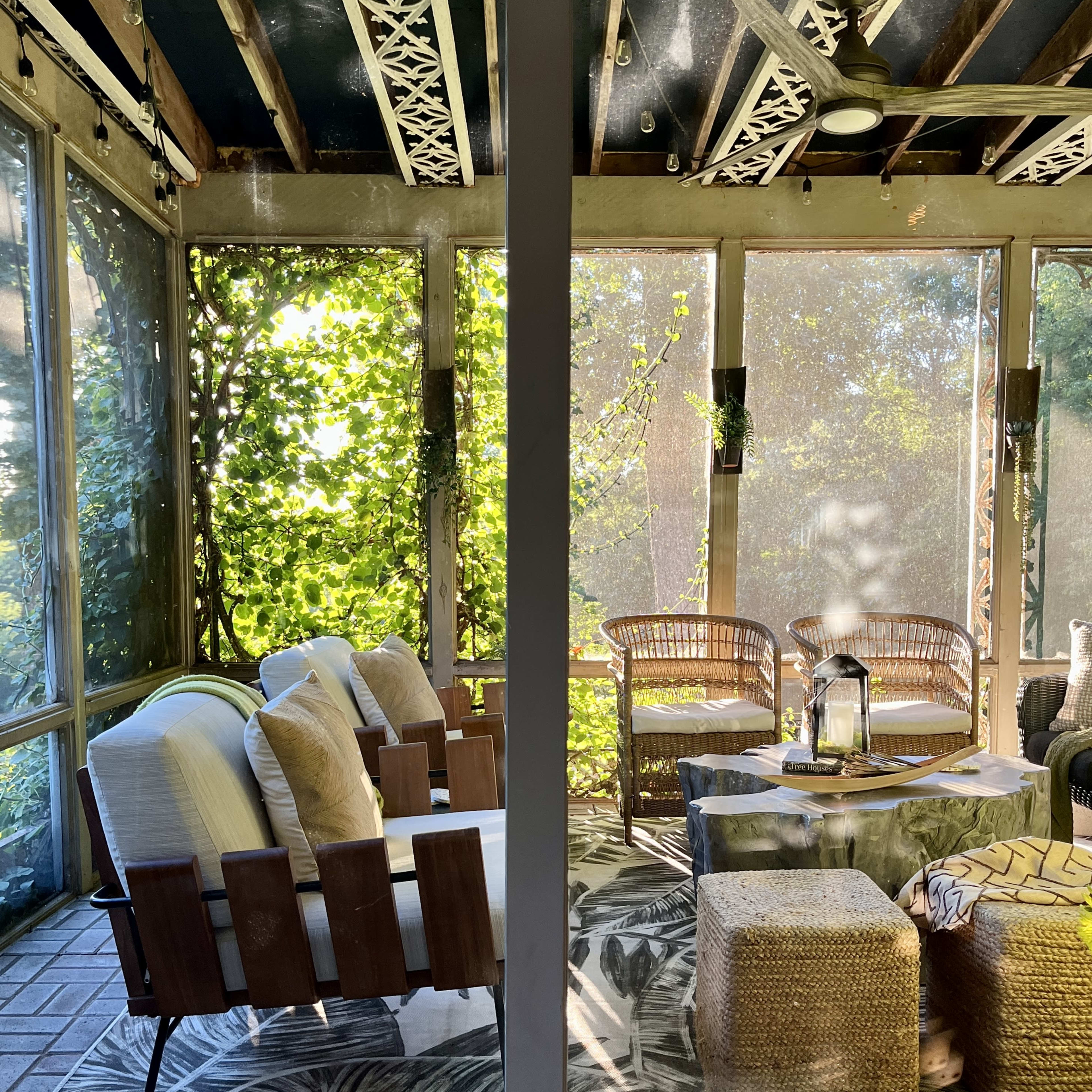 A screened-in porch with wooden chairs, a table, and a lush green backdrop.