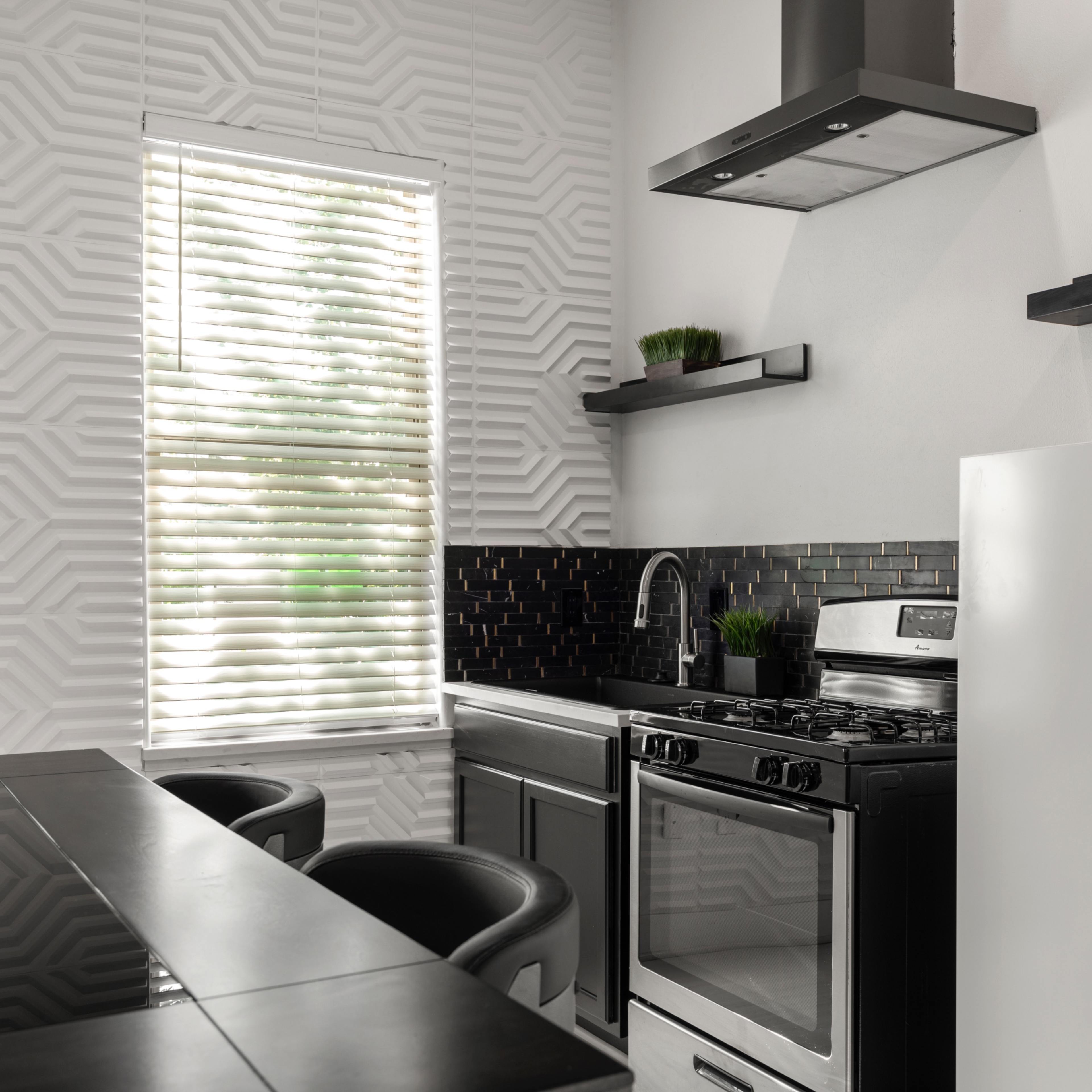 A modern kitchen features a black countertop, silver appliances, and geometric white wall patterns.