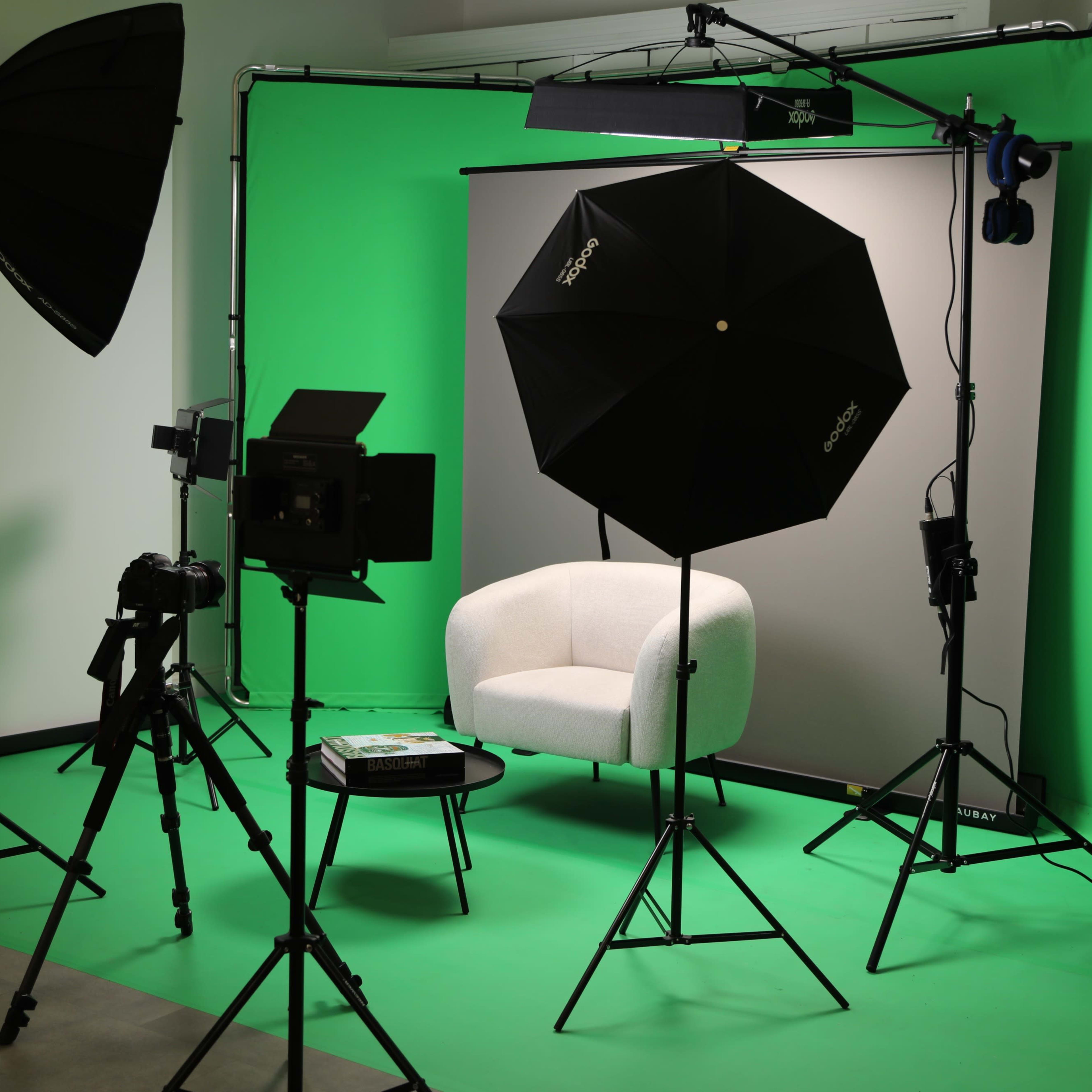 A studio setup featuring a white chair, backdrop, lighting equipment, and cameras on green flooring.