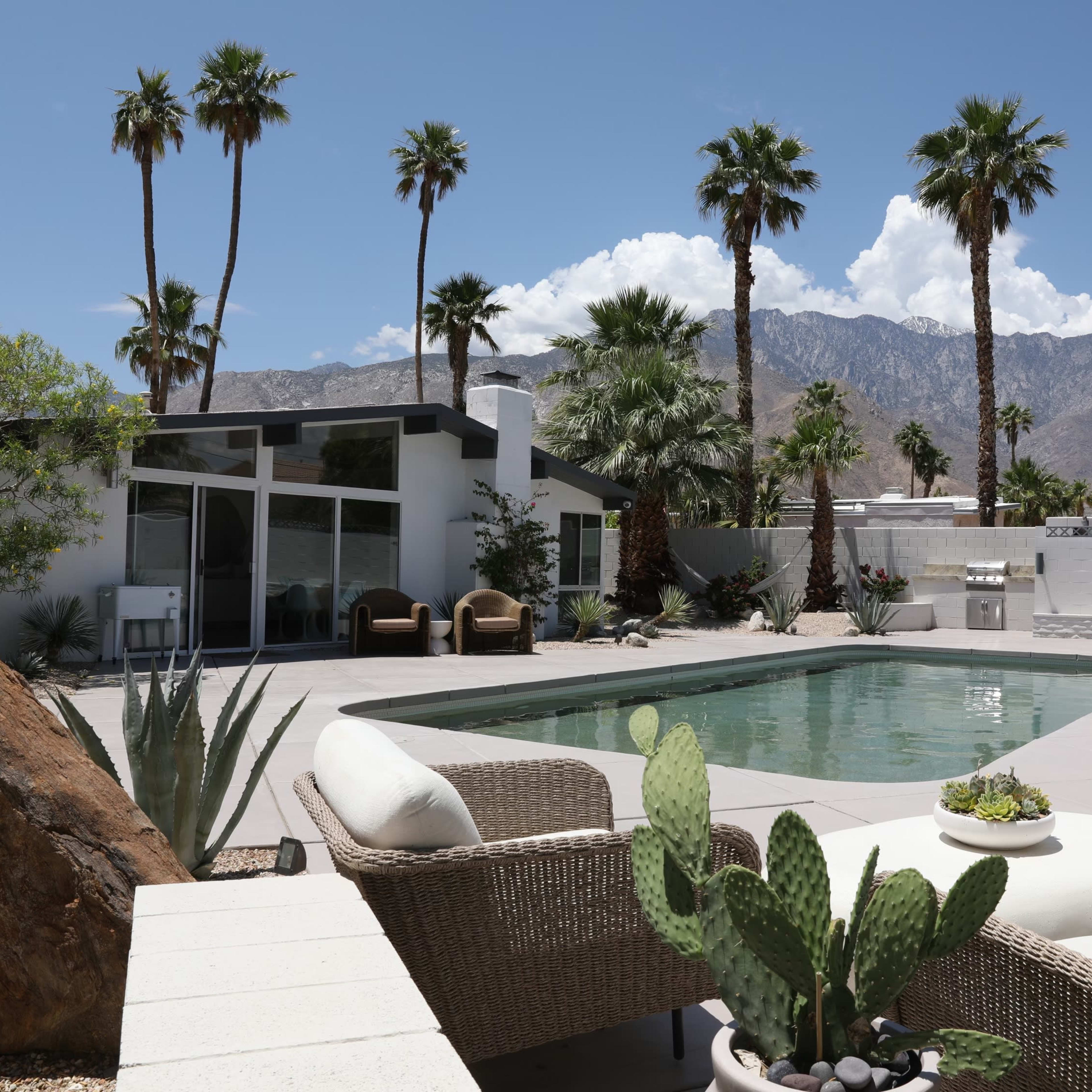 A modern house with a swimming pool, surrounded by palm trees and mountains in the background.