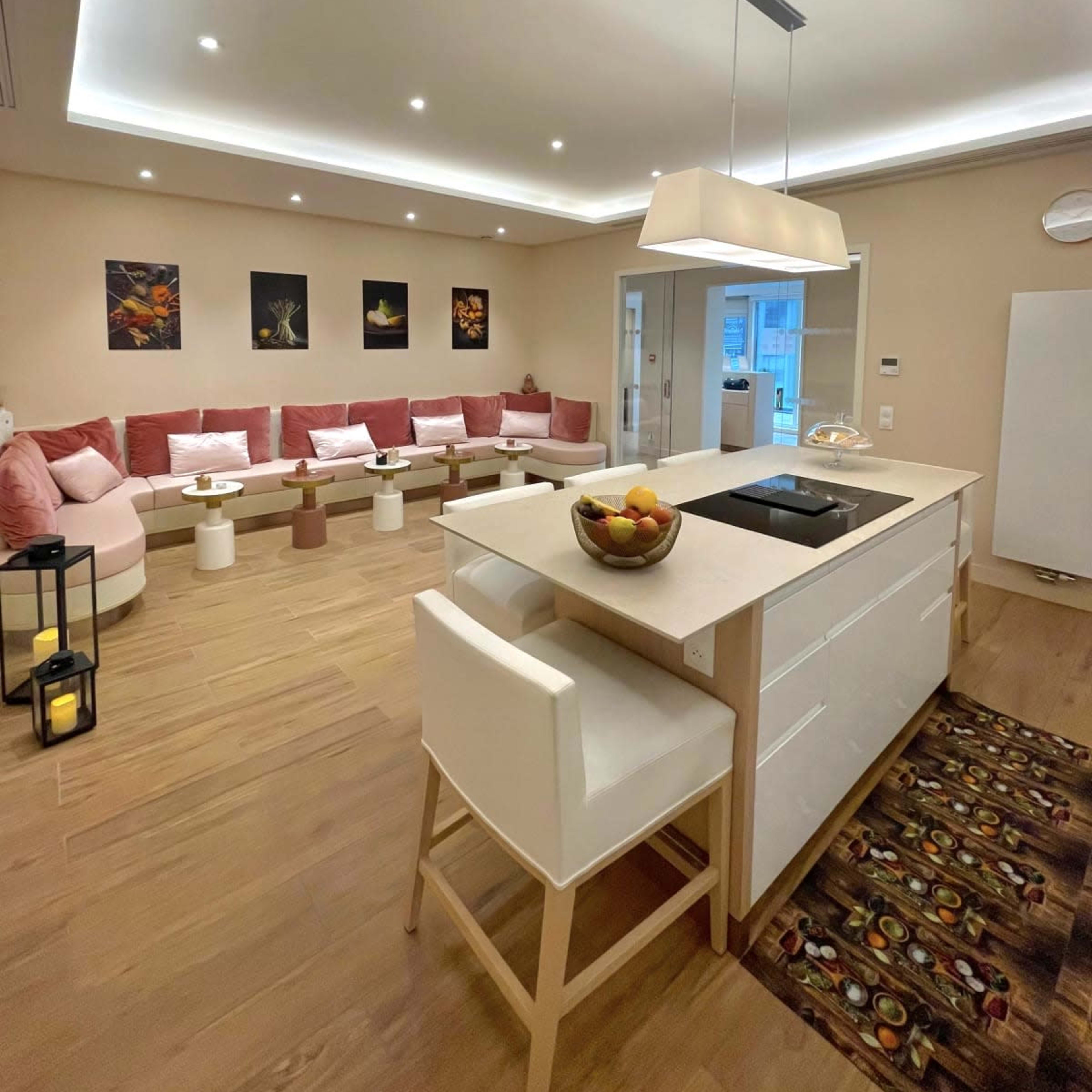 A modern, open-concept living space featuring a kitchen island with seating, a seating area with pink cushions, and decorative wall art.