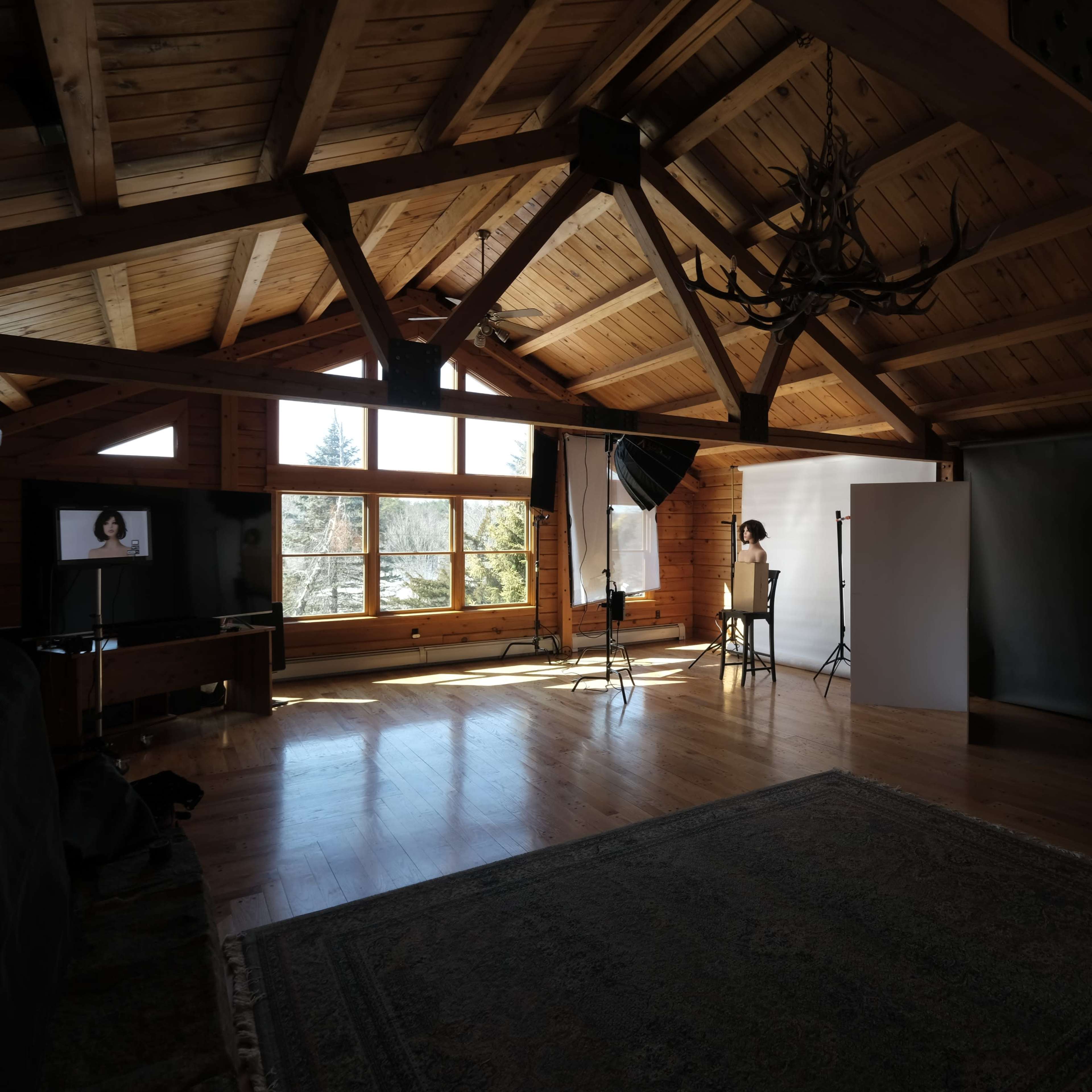 A spacious, rustic studio with wooden beams, large windows, and photography equipment set up in an illuminated area.