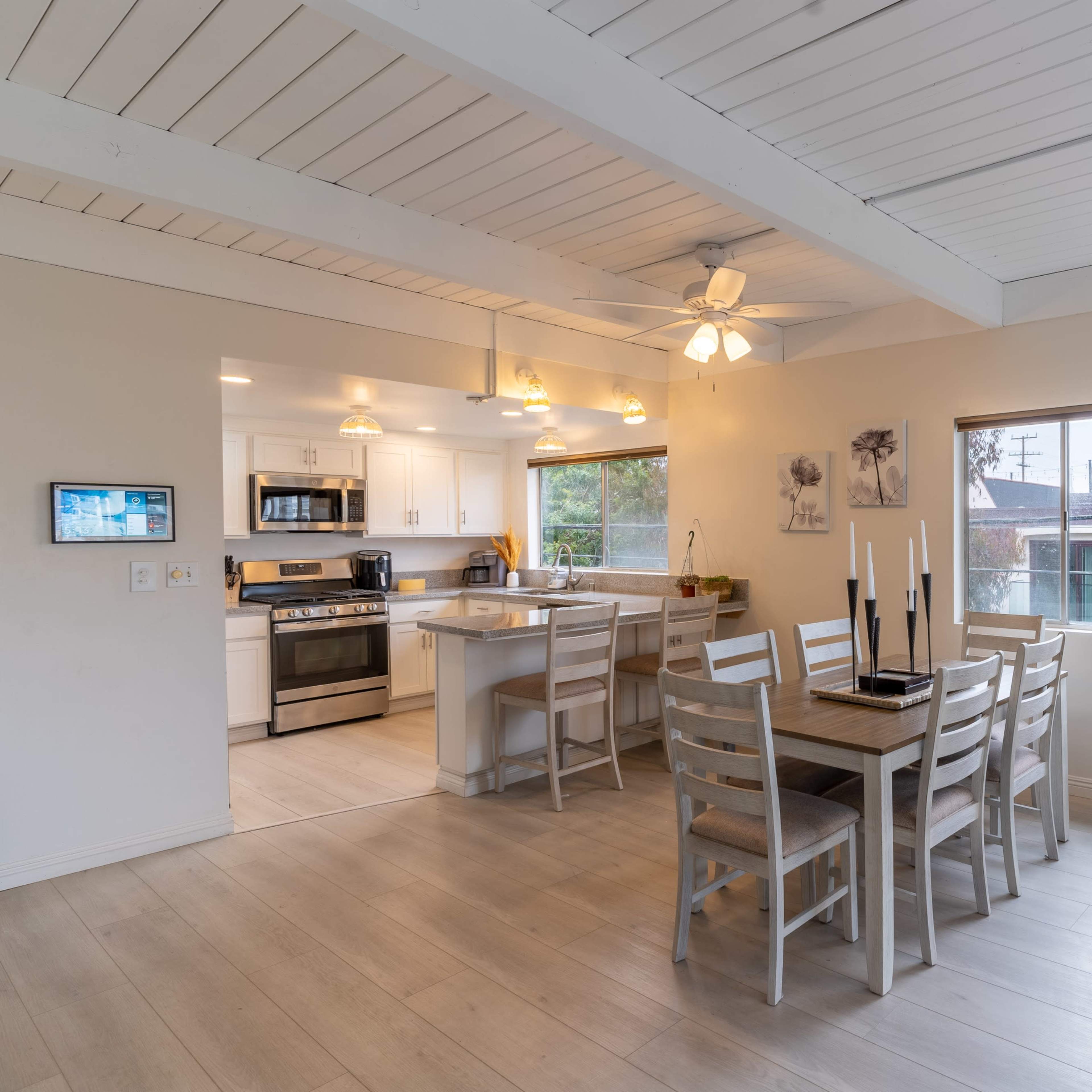 A bright, open living space features a dining area with a table and chairs adjacent to a modern kitchen, all illuminated by overhead lighting.