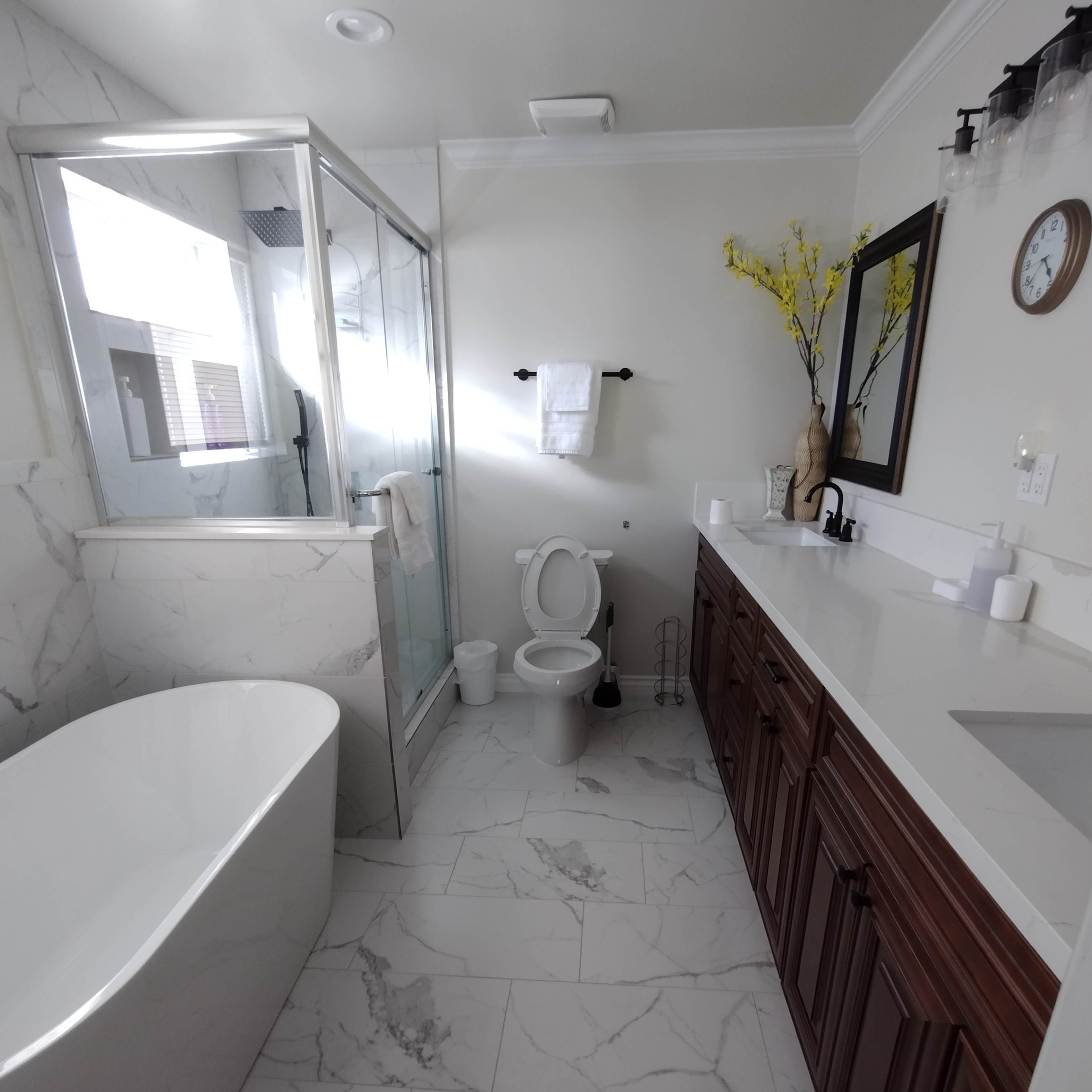 A modern bathroom featuring a freestanding bathtub, a glass shower enclosure, a toilet, and a double sink vanity with wooden cabinetry.