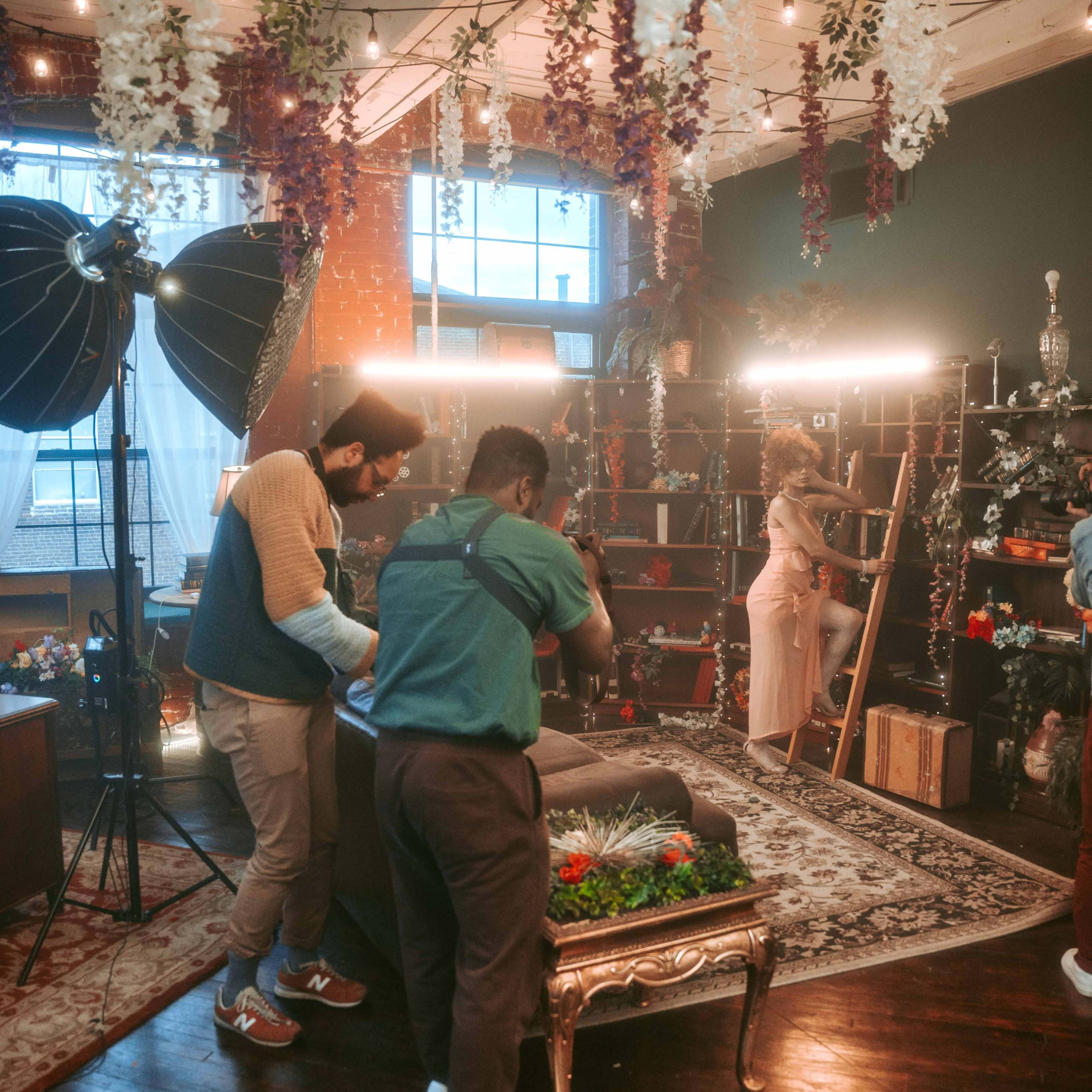 A photoshoot is underway in a well-decorated studio with lighting equipment and floral decorations.