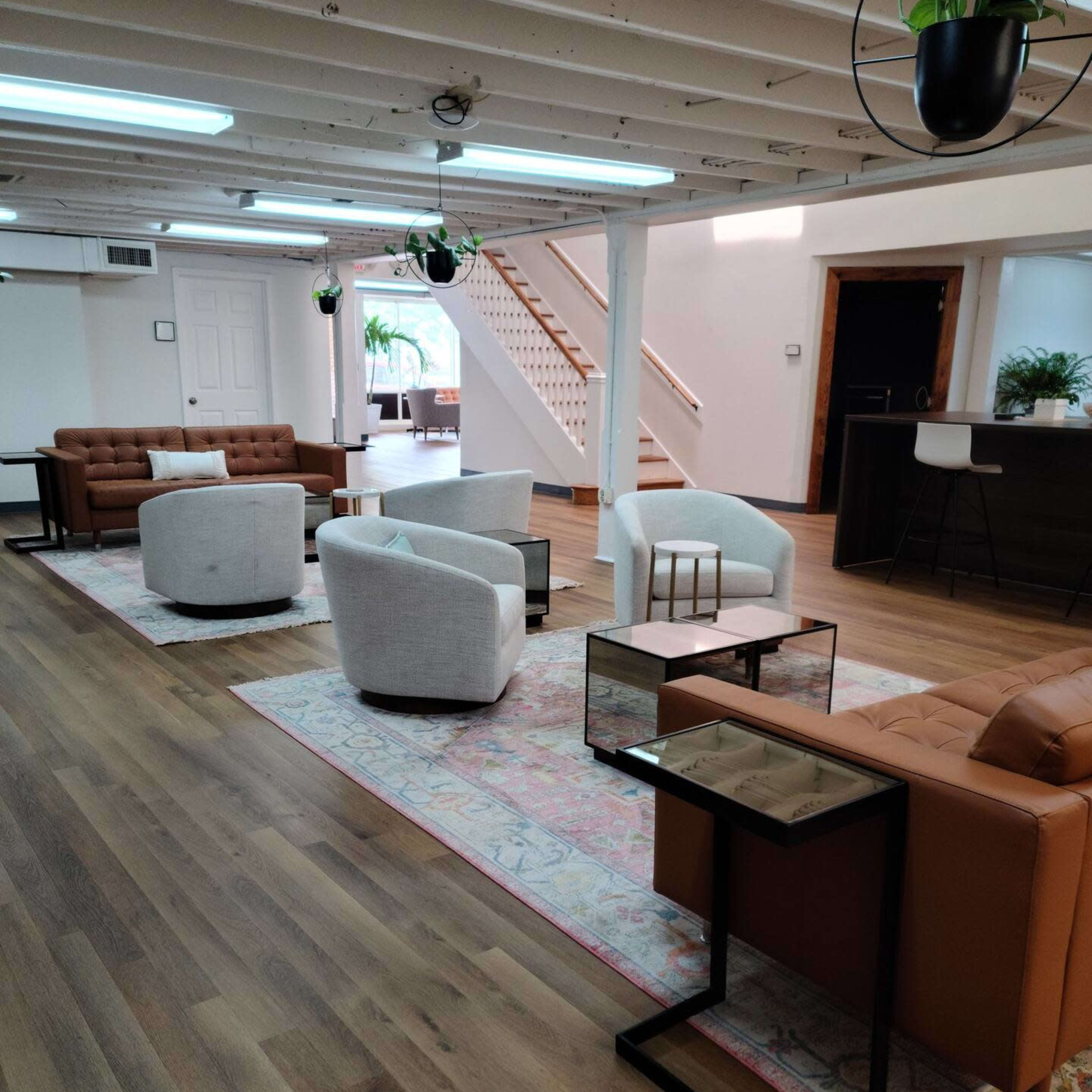 A spacious lounge area with several modern seating arrangements, including sofas and armchairs, set on a wooden floor, with decorative rugs and plants.