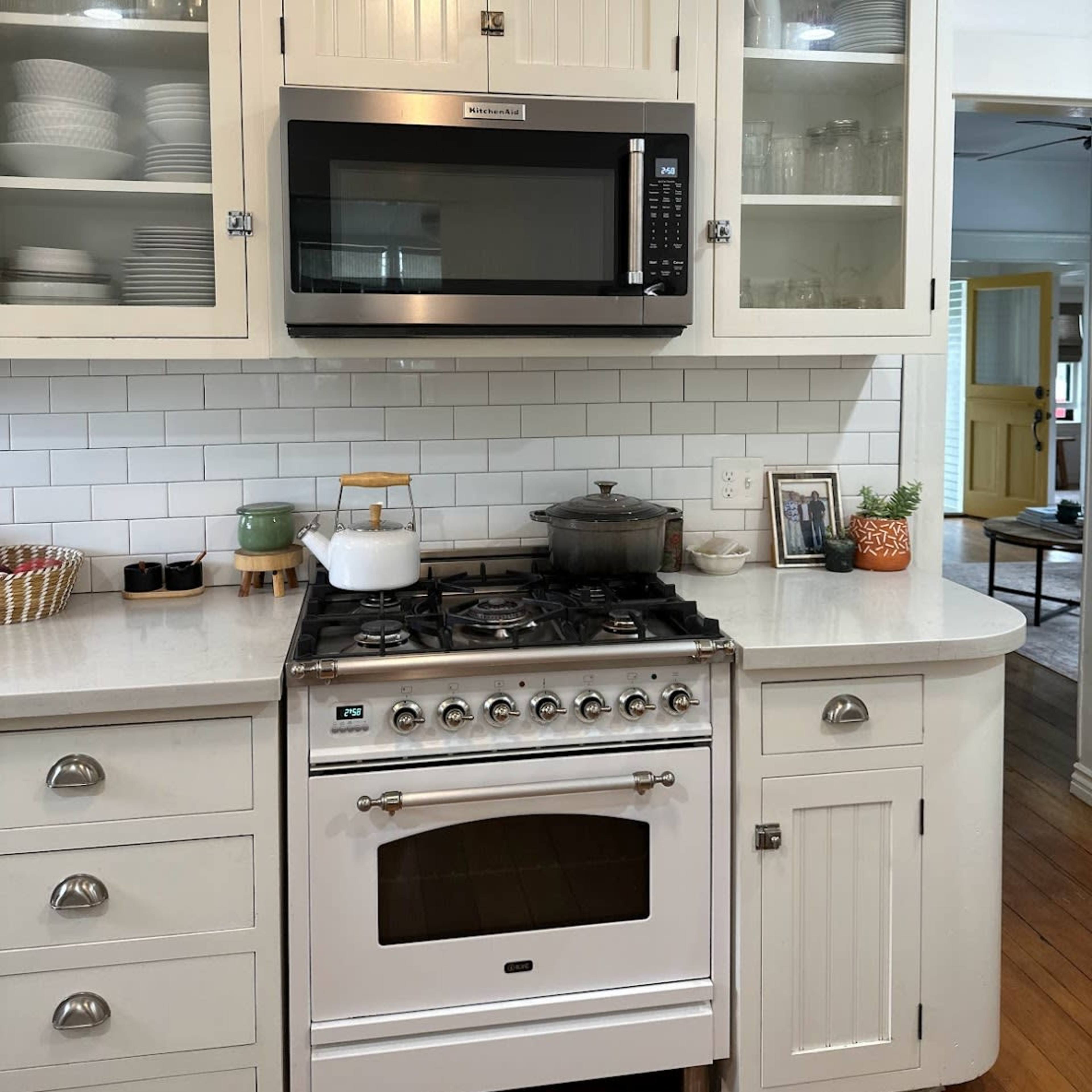 A kitchen featuring a white gas stove, a microwave mounted above it, and cabinets with glass doors displaying dishware.