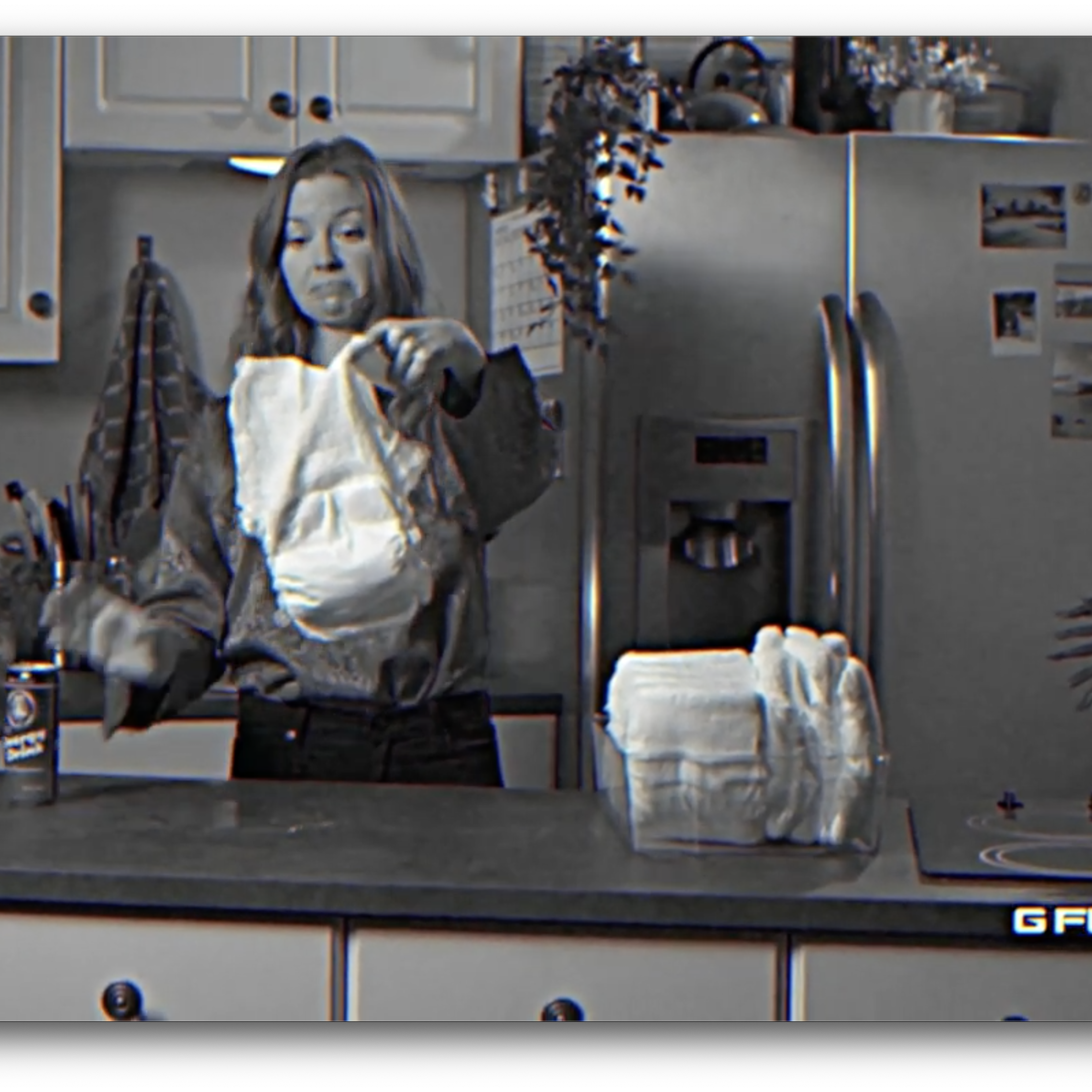 A person is holding a diaper in a kitchen while standing next to a stack of diapers and a can of G Fuel on the counter.