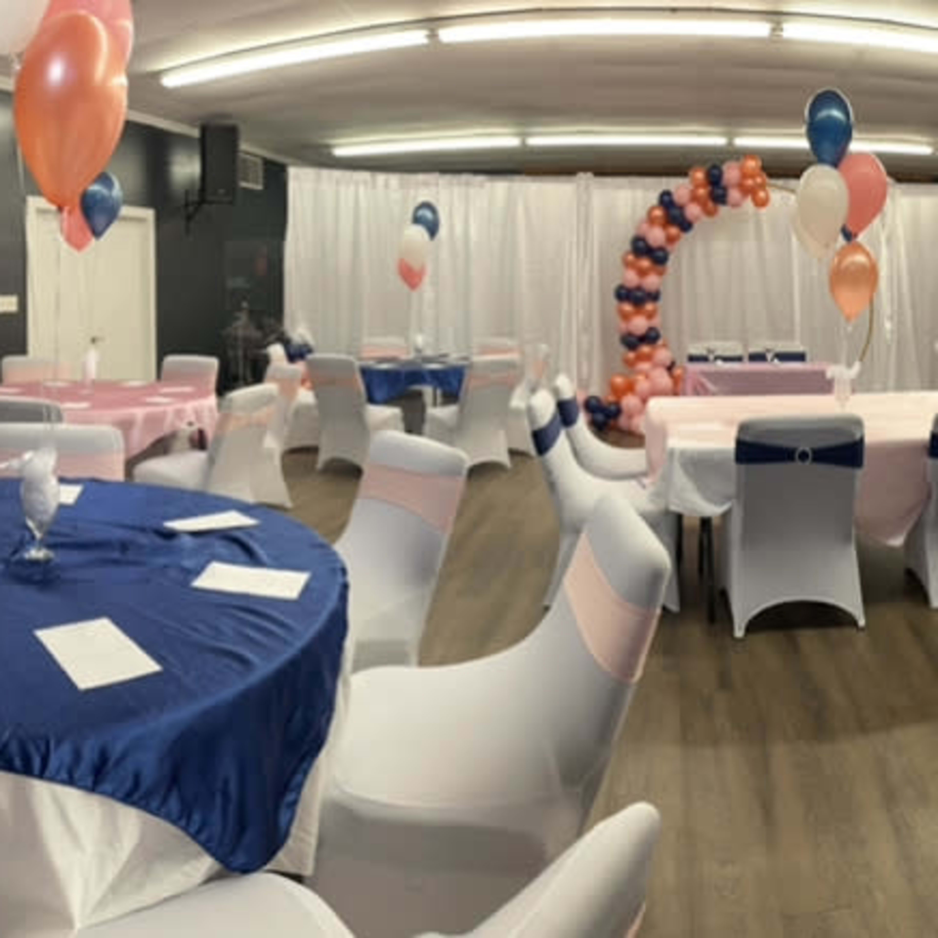 A decorated event space with tables covered in pastel linens, balloons, and an arch made of balloons.