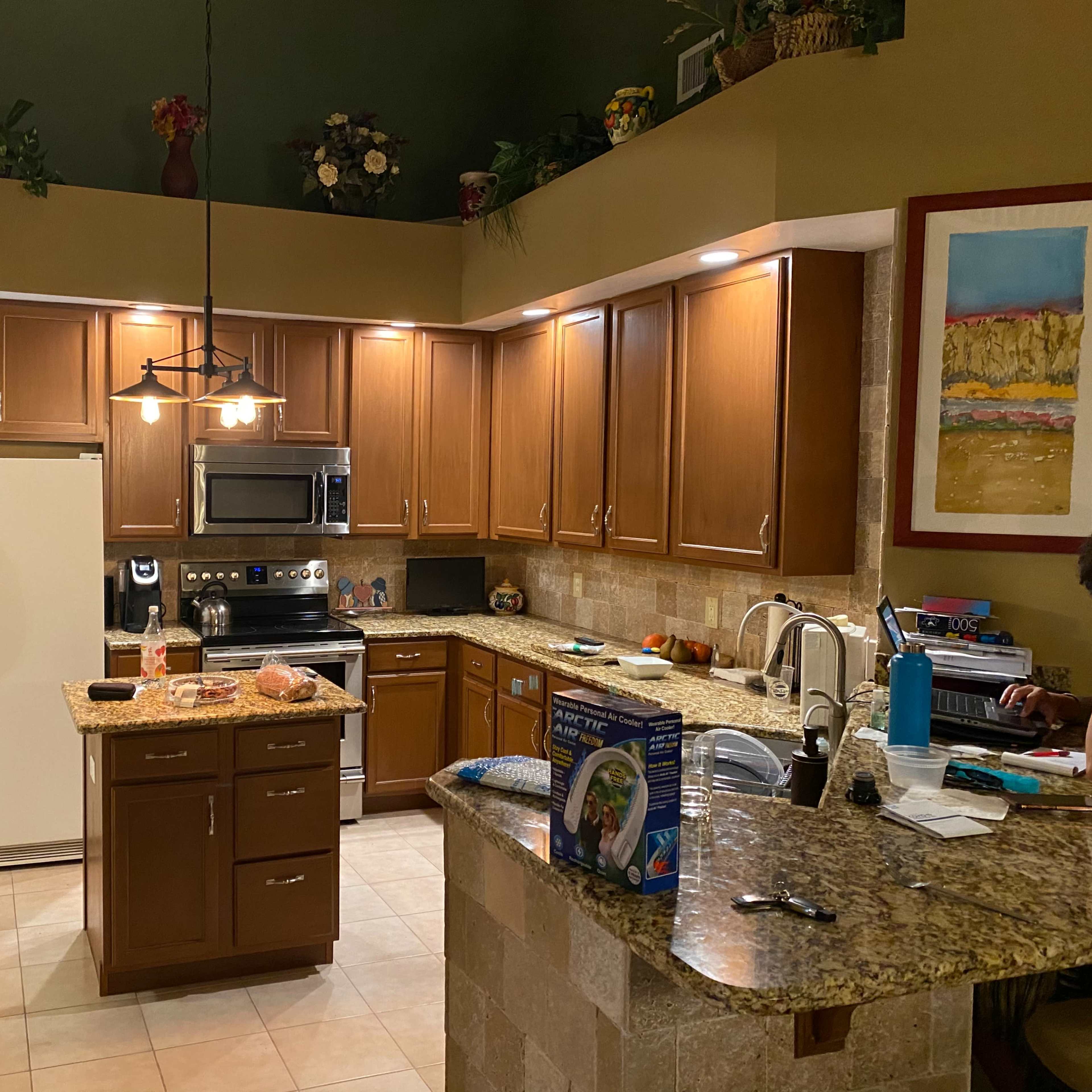 A modern kitchen with wooden cabinets, a large central island, and various appliances including a refrigerator and oven, all situated within a well-lit space.