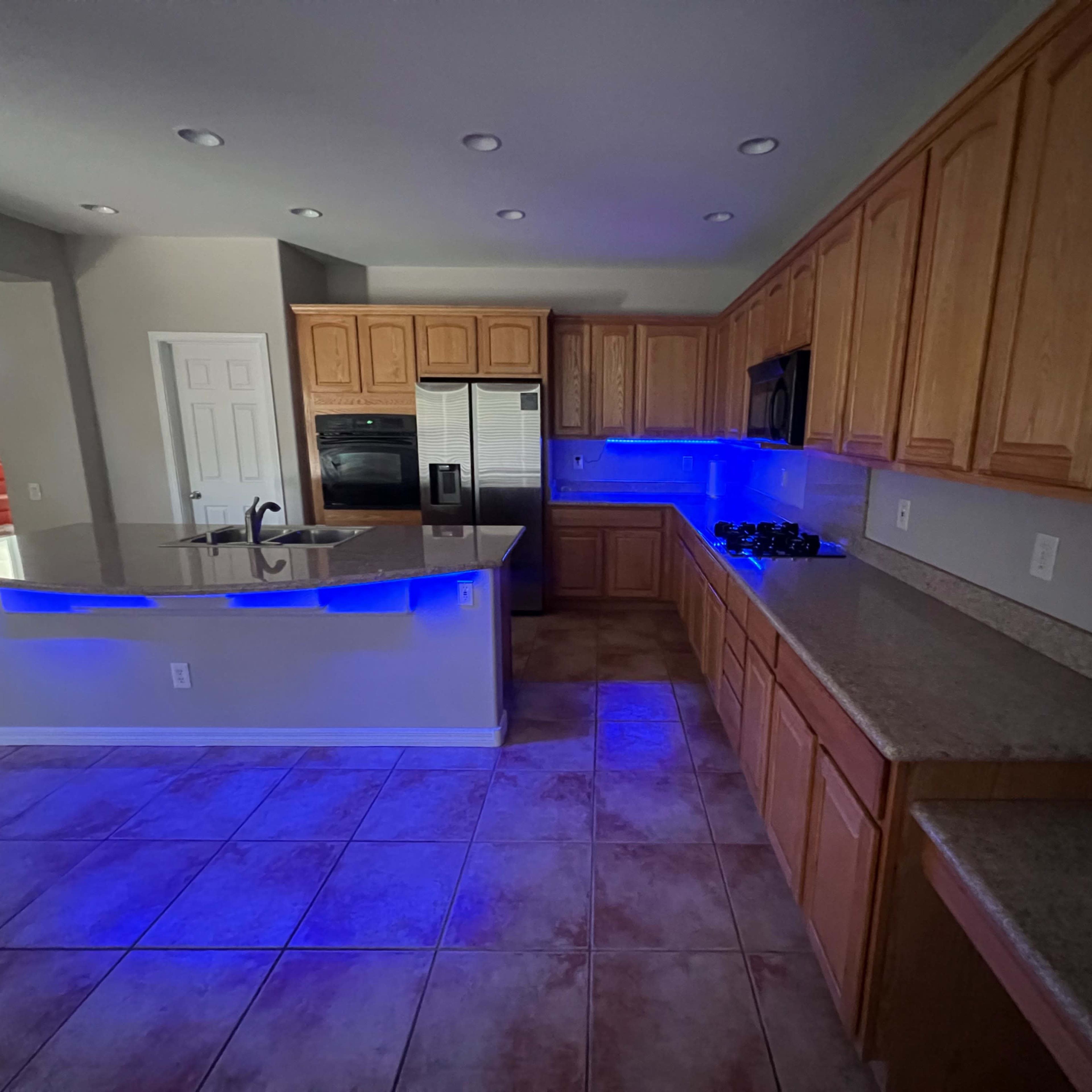 The kitchen features wooden cabinetry, a spacious island, and blue LED lighting along the countertops.