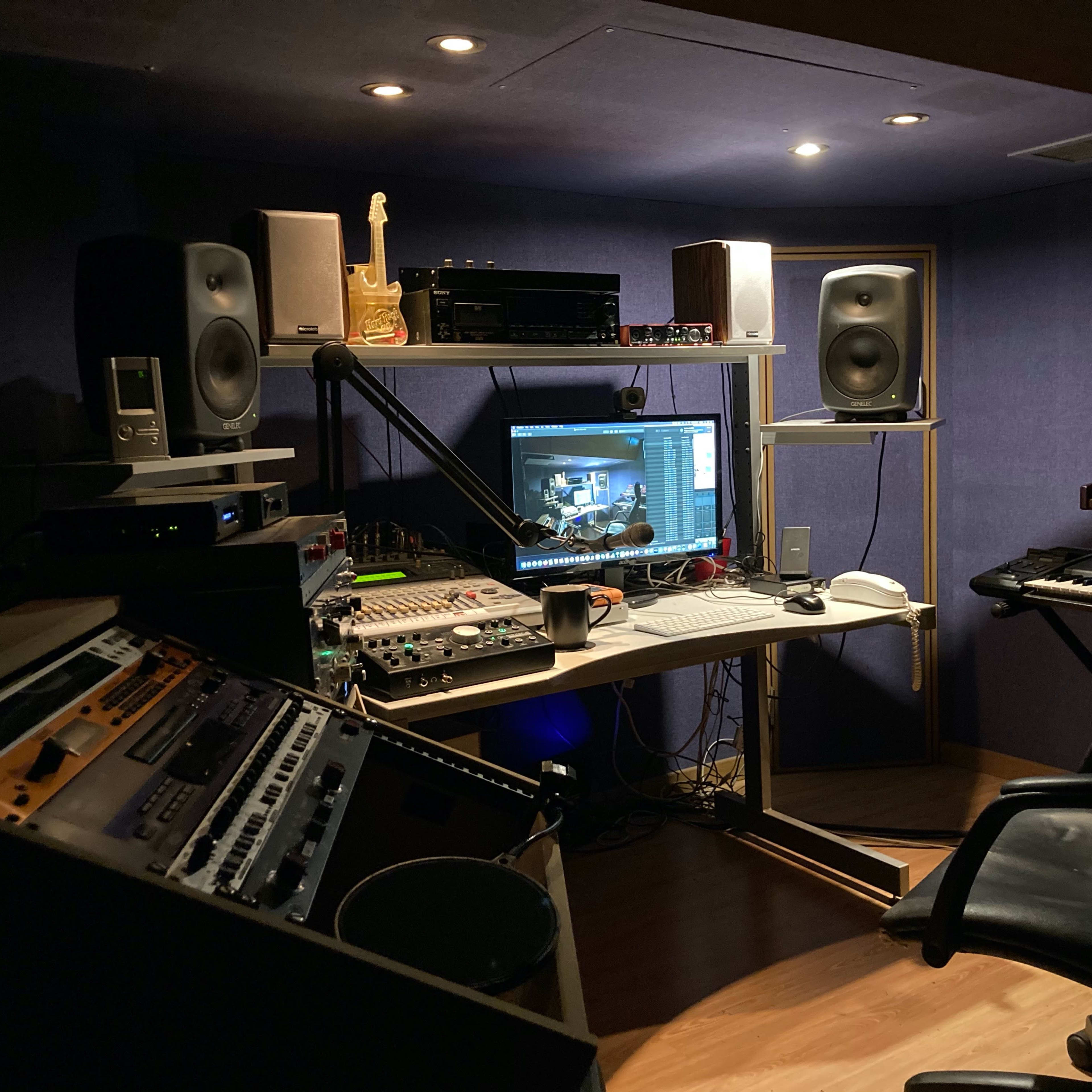 A music studio setup featuring a computer workstation, audio equipment, synthesizers, and studio monitors arranged in a compact space.