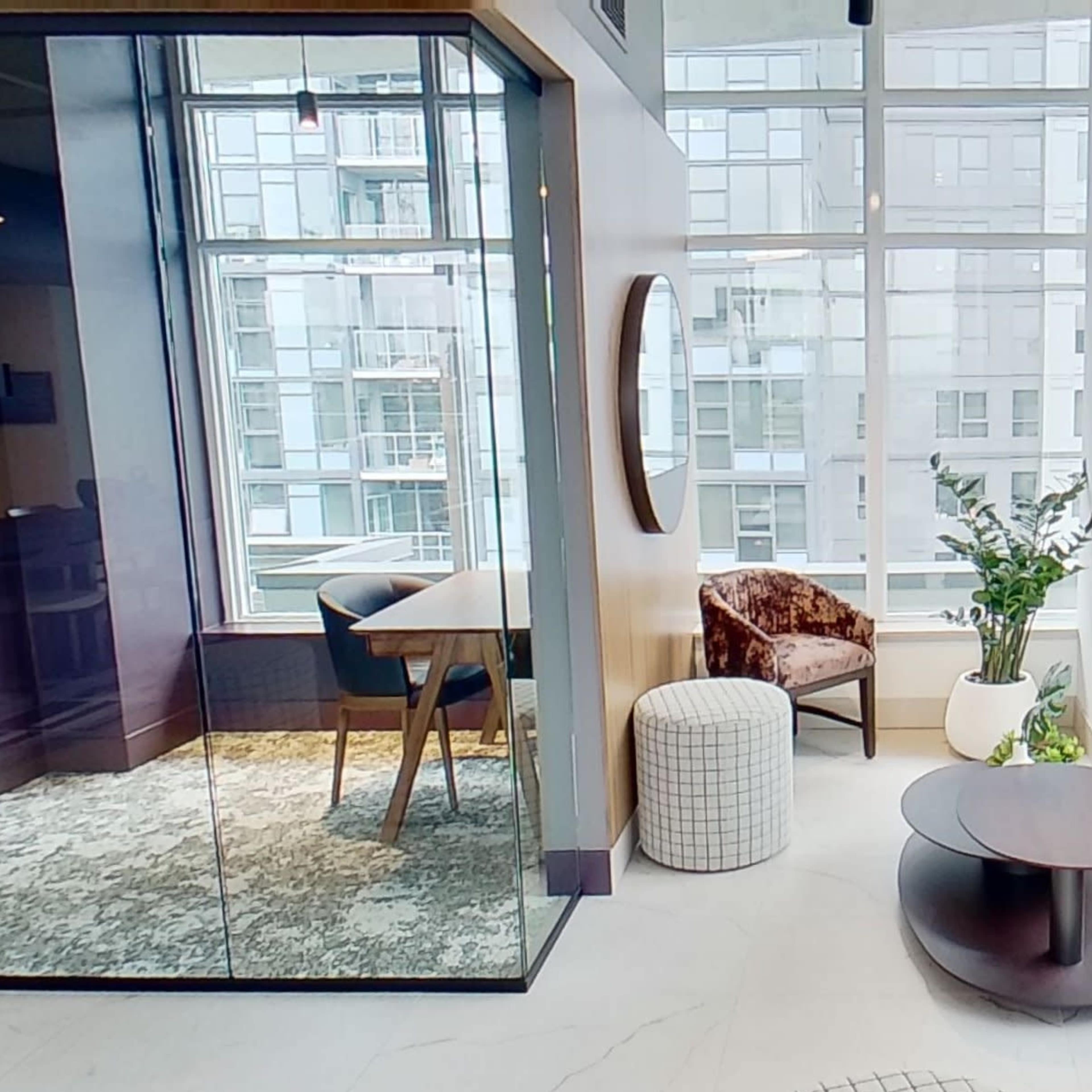 A modern interior with a seating area featuring a curved sofa, a round coffee table, and a glass-walled meeting room illuminated by natural light from large windows.