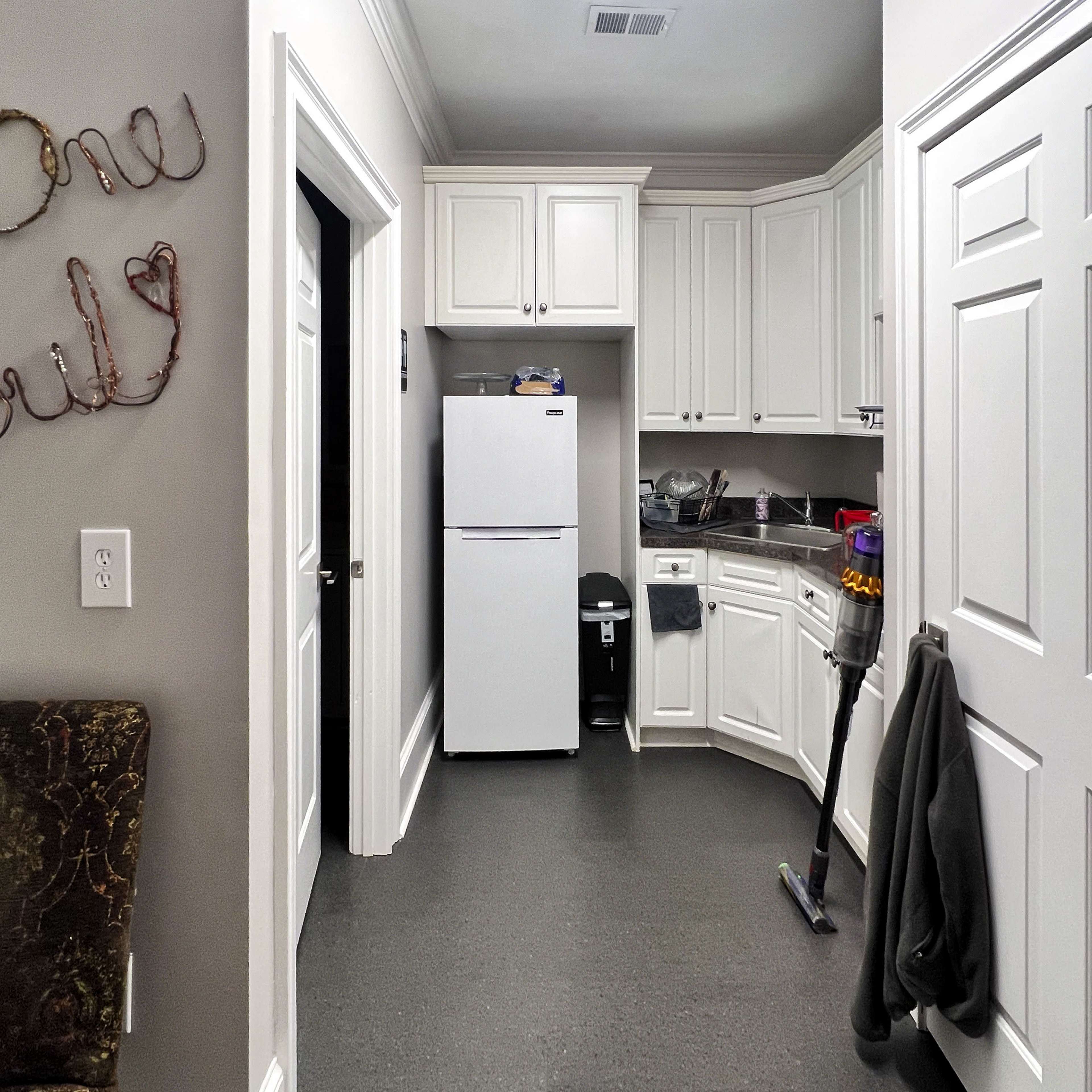 A small kitchen area features white cabinets, a refrigerator, and a doorway leading to another room.