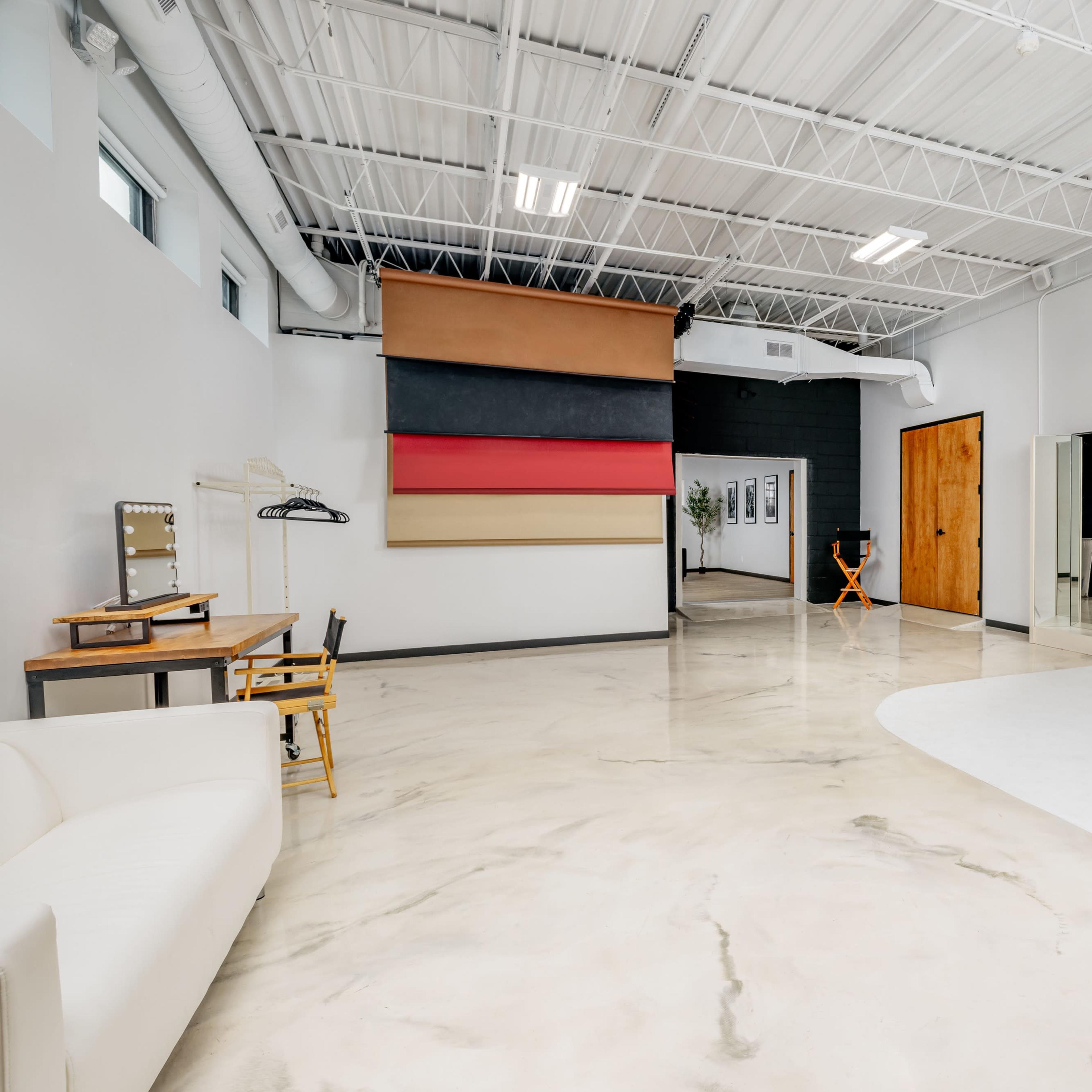 A spacious photography studio featuring a seamless backdrop, a seating area, and a changing room.