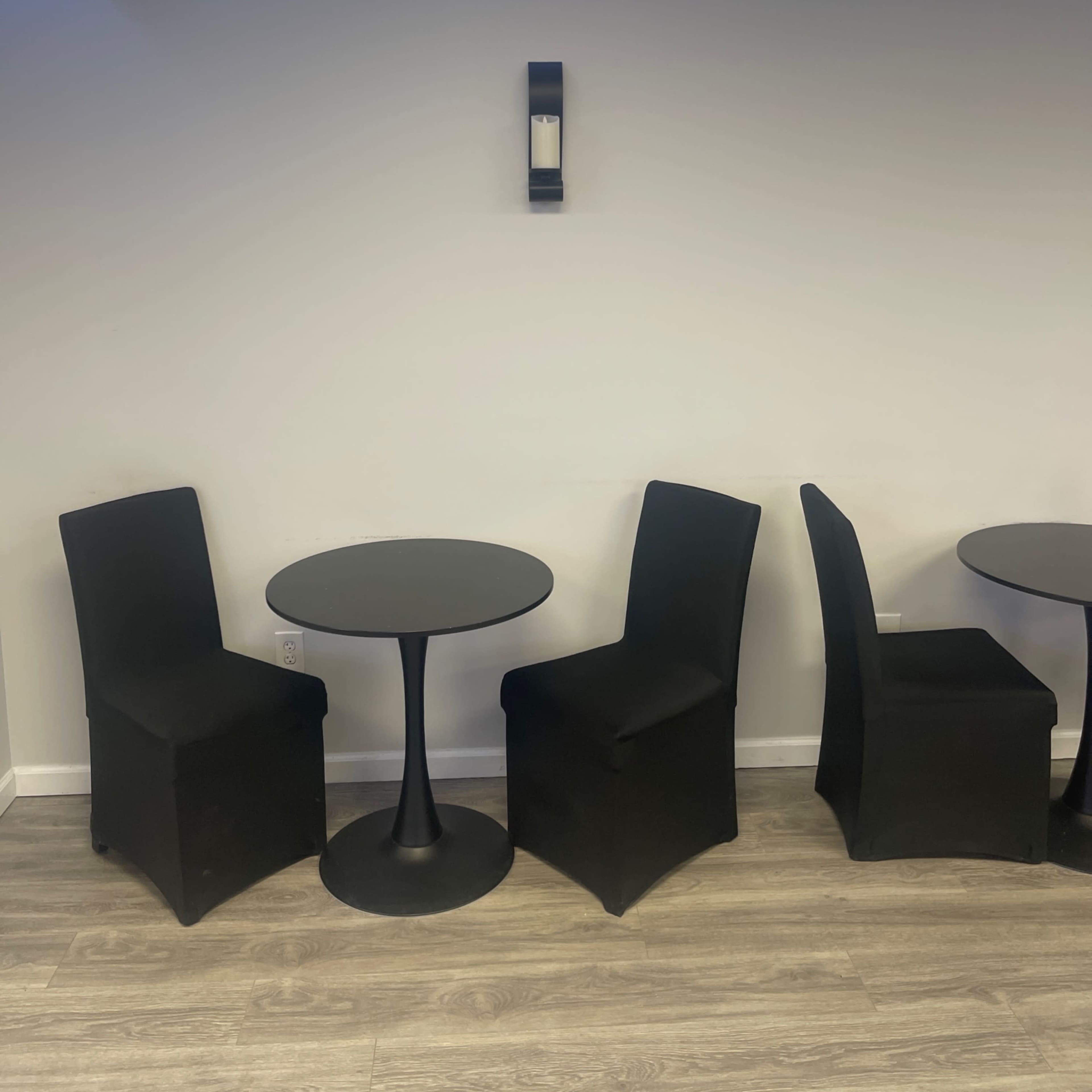 A small black table with four matching chairs is set against a white wall, illuminated by blue lighting above.