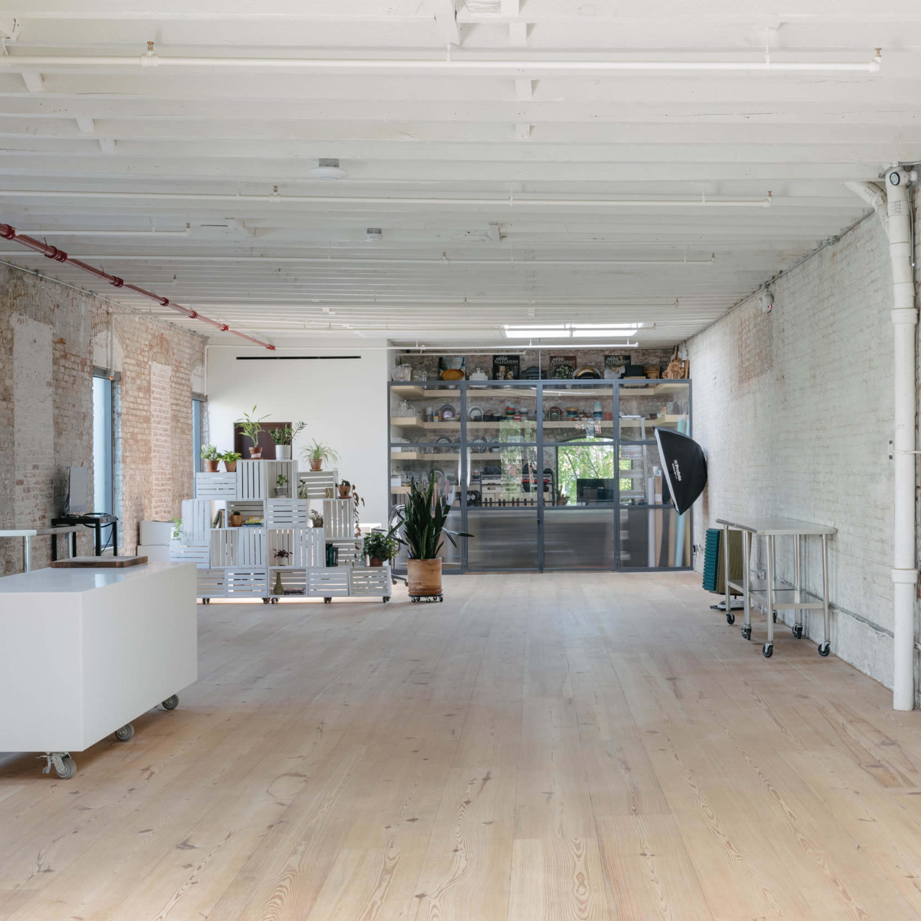 A spacious, well-lit room with wooden floors, white brick walls, and a large glass display cabinet against one wall.