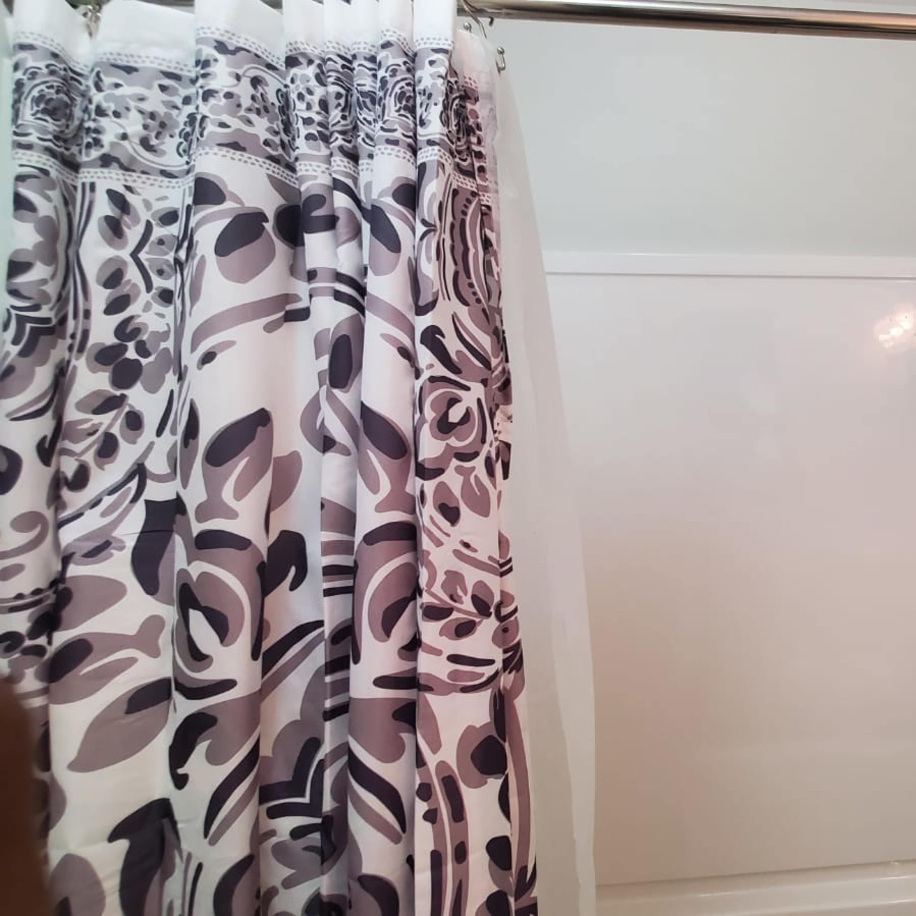 A shower area with a patterned curtain, a showerhead, and a smooth, white tub enclosure.