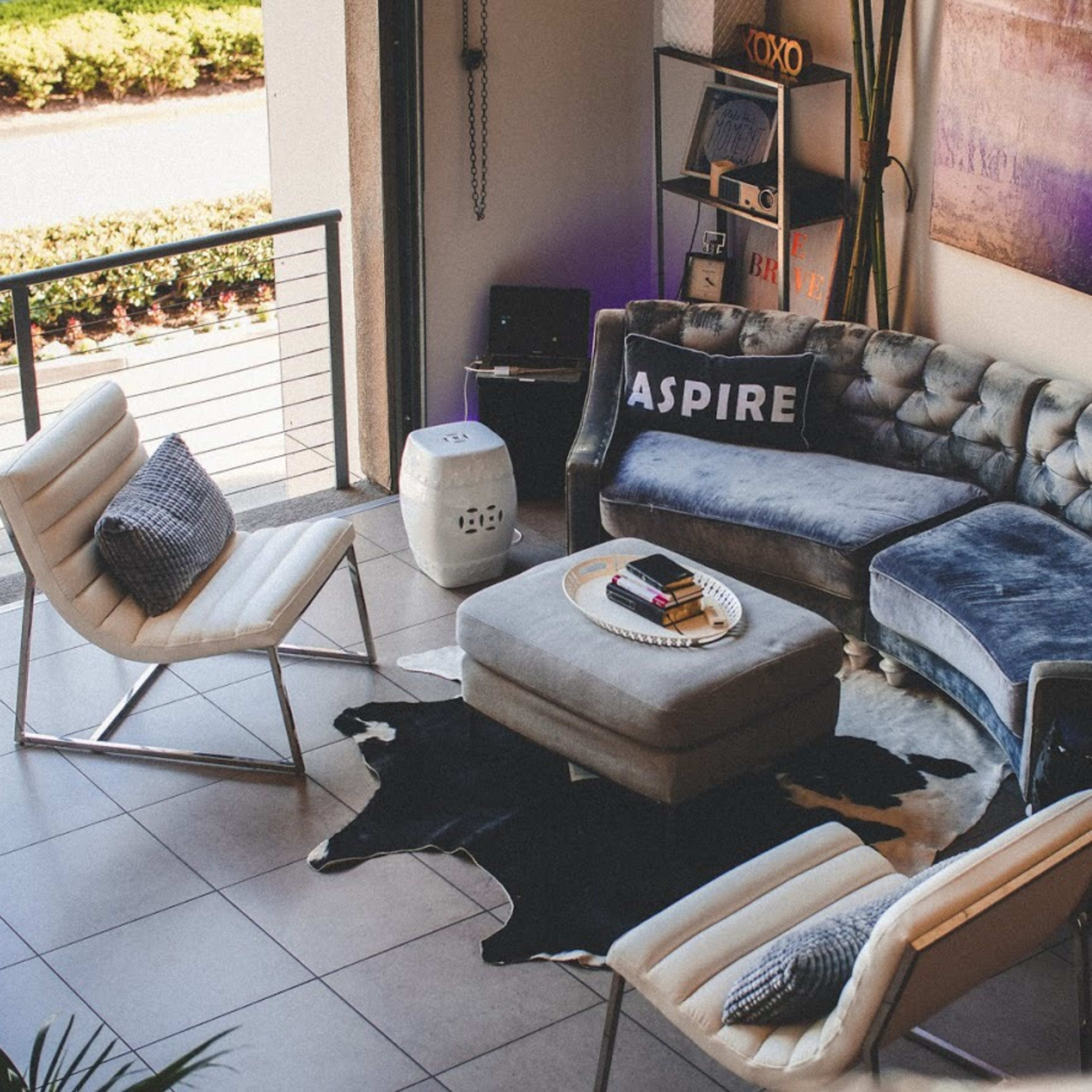 A modern living room with a tufted blue sectional sofa, two white chairs, a round coffee table, and a black and white cowhide rug.