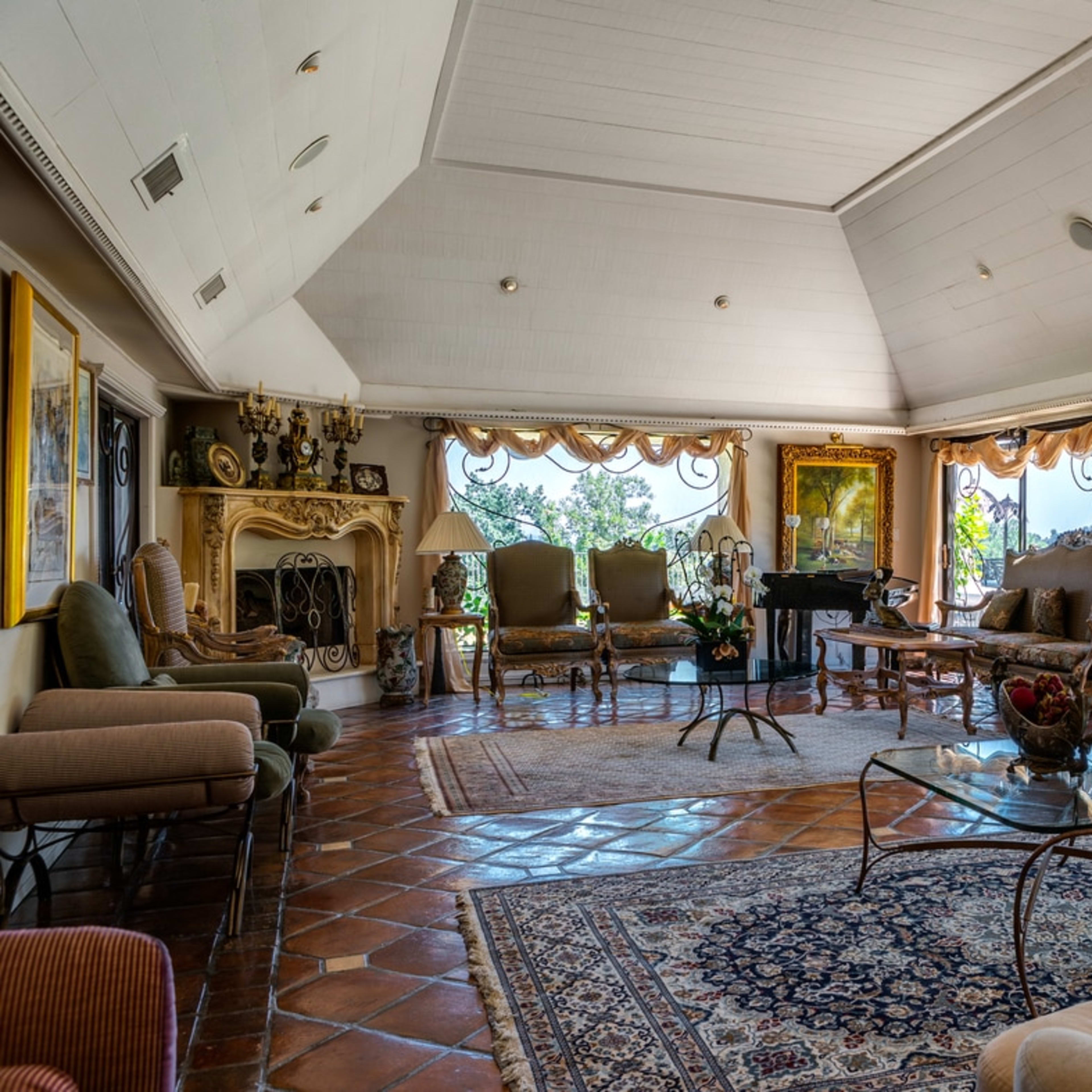 A spacious living room with large windows, a decorative fireplace, and a mix of elegant furniture arranged around a glass coffee table.
