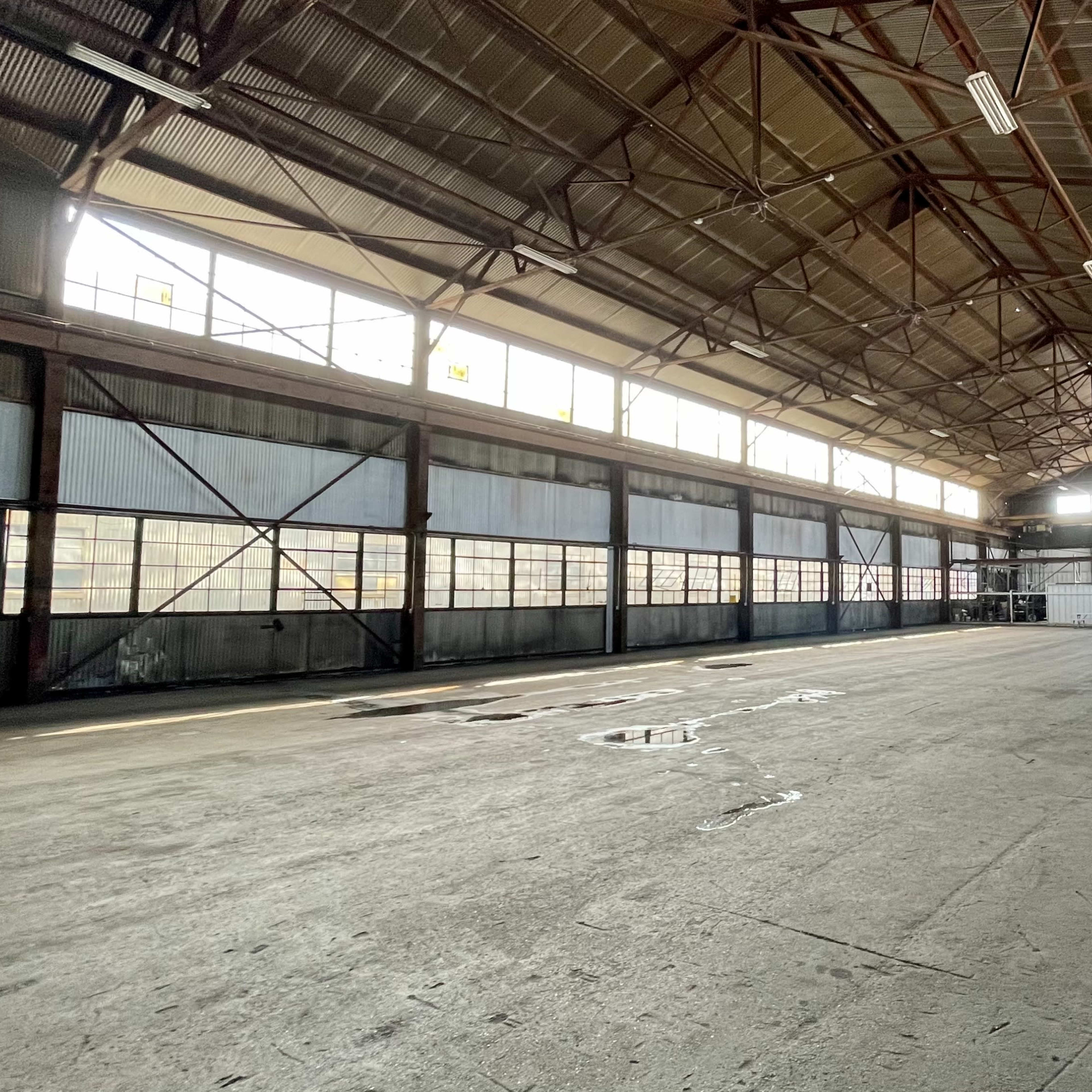 A spacious, industrial warehouse with high ceilings, large windows, and a concrete floor.