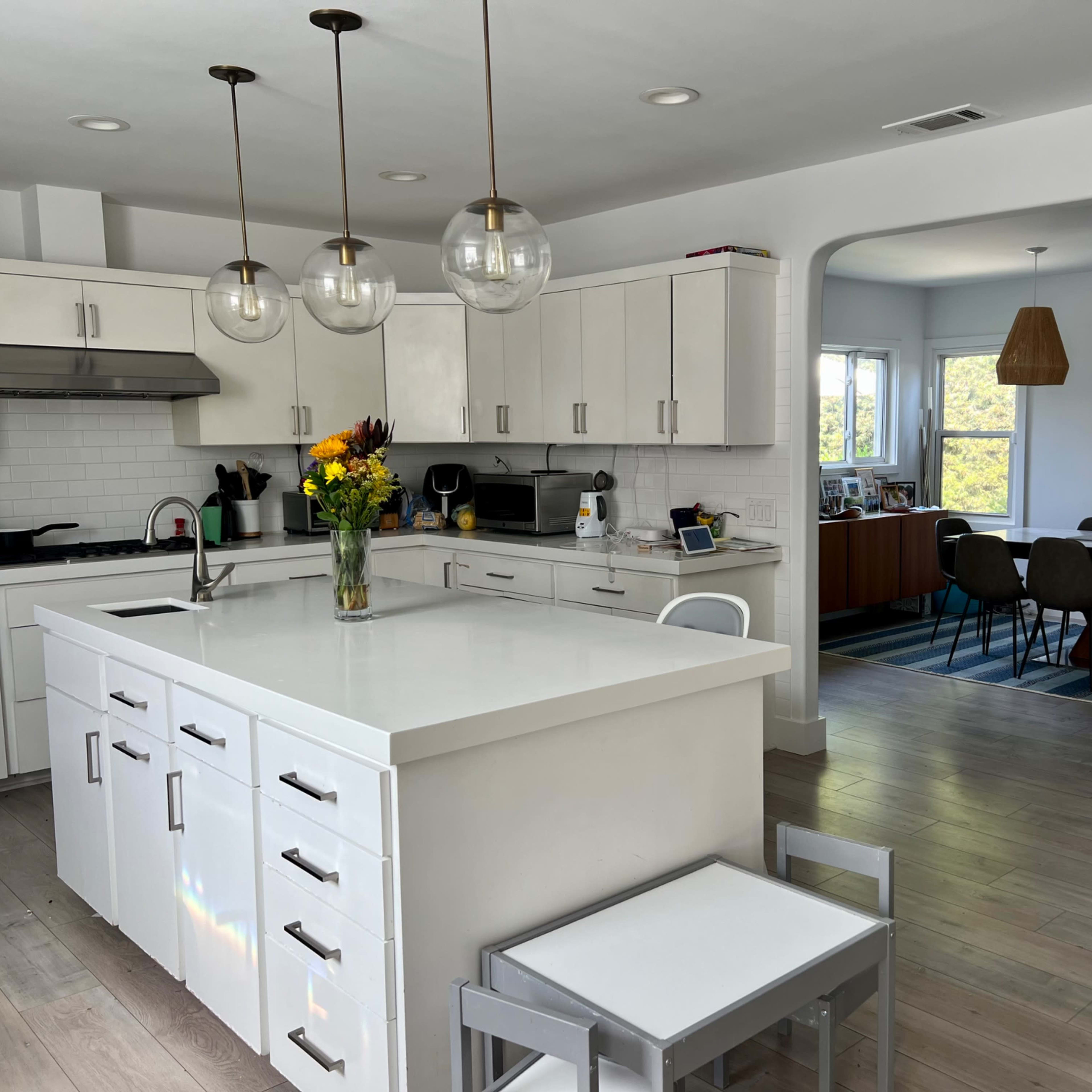 A modern kitchen features white cabinetry, a large island with a sink, and a dining area visible through an archway.