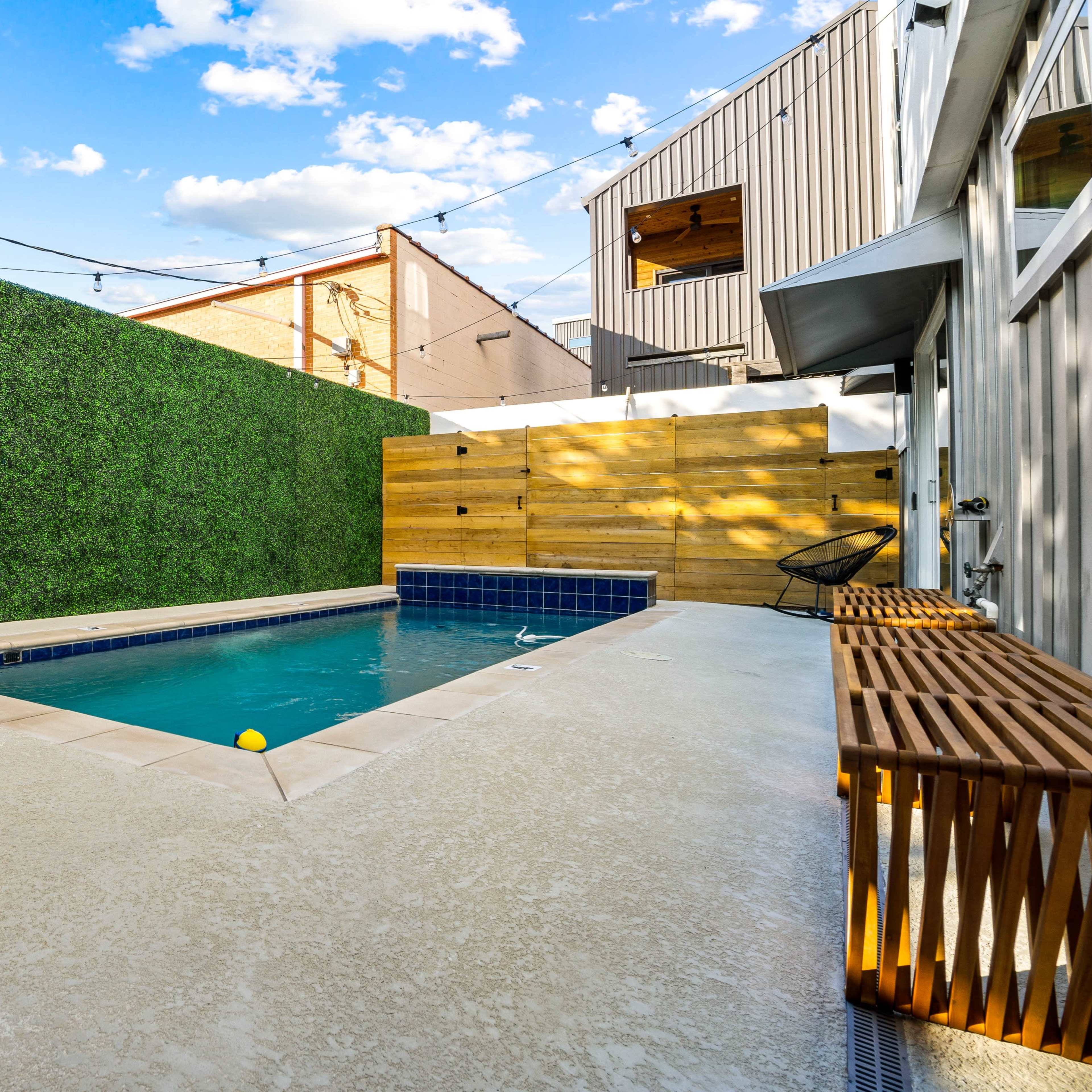 A backyard pool area with a lounge chair, surrounded by green walls and wooden fencing.