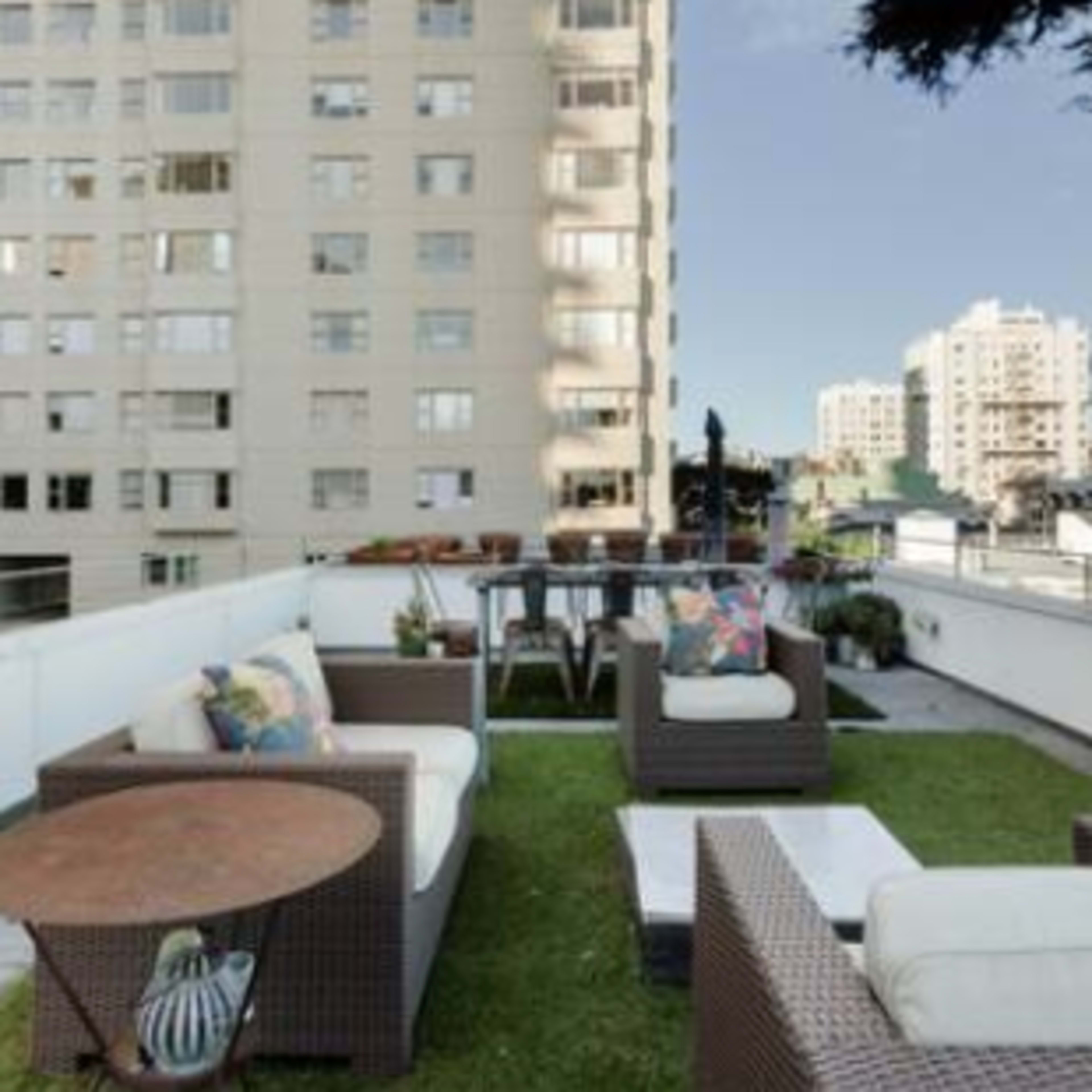 A terrace featuring outdoor furniture, including sofas and a coffee table, overlooking a cityscape with several buildings.