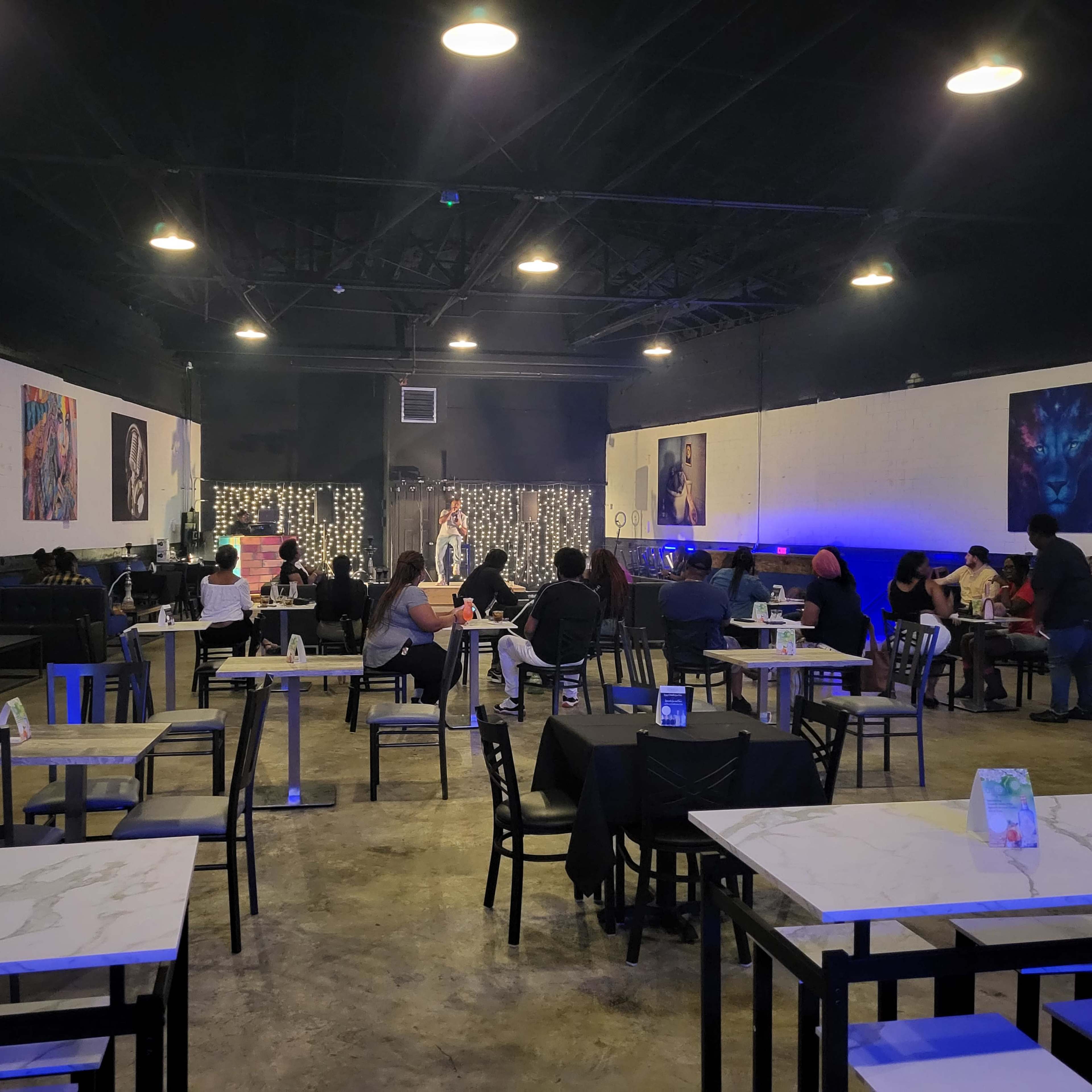 A performance is taking place in a dimly lit venue with chairs and tables arranged for an audience.