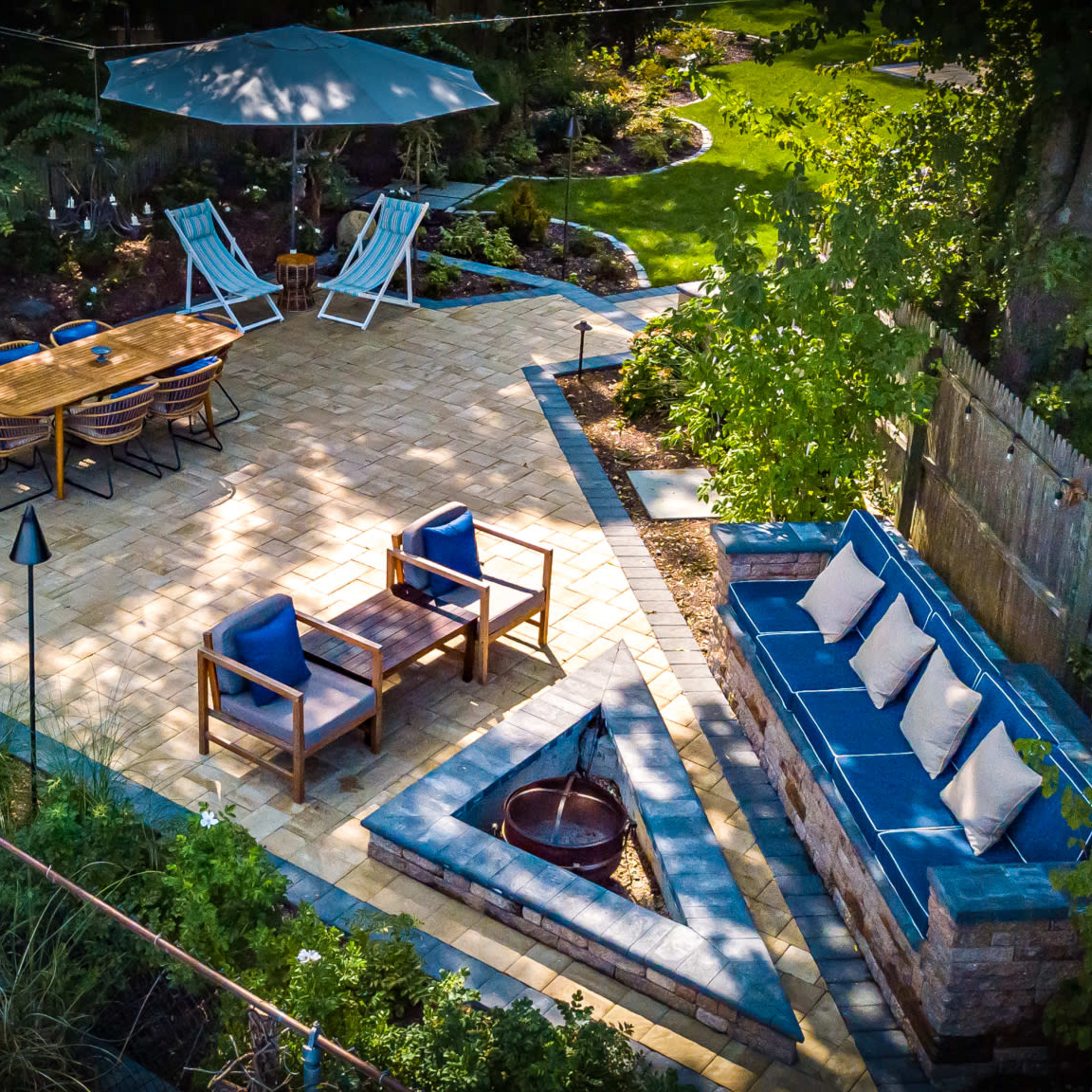 A landscaped patio area featuring outdoor seating, a dining table, and a fire pit surrounded by greenery.