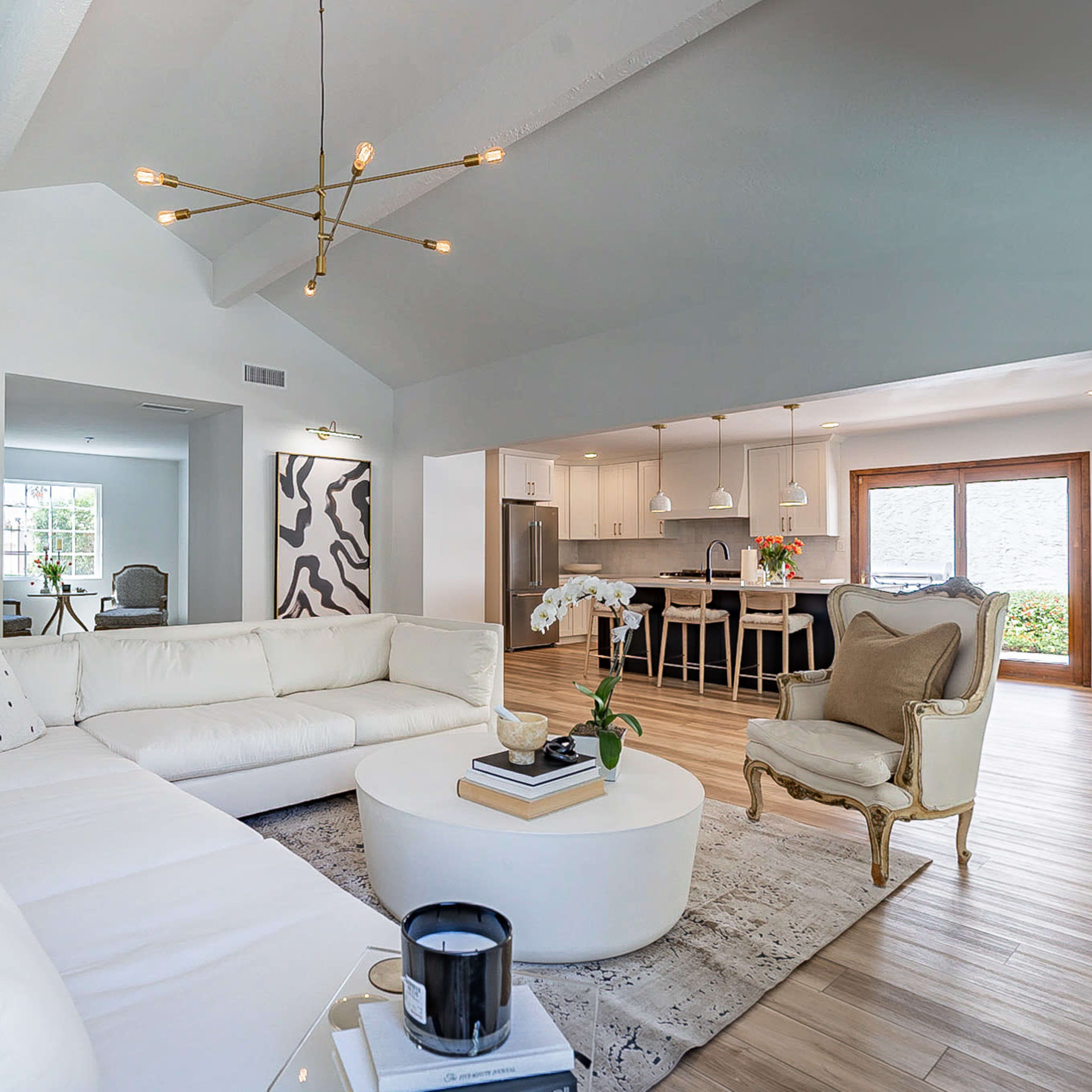 A modern living room with a white sectional sofa, a round coffee table, and a view into an adjoining kitchen area with a dining table.