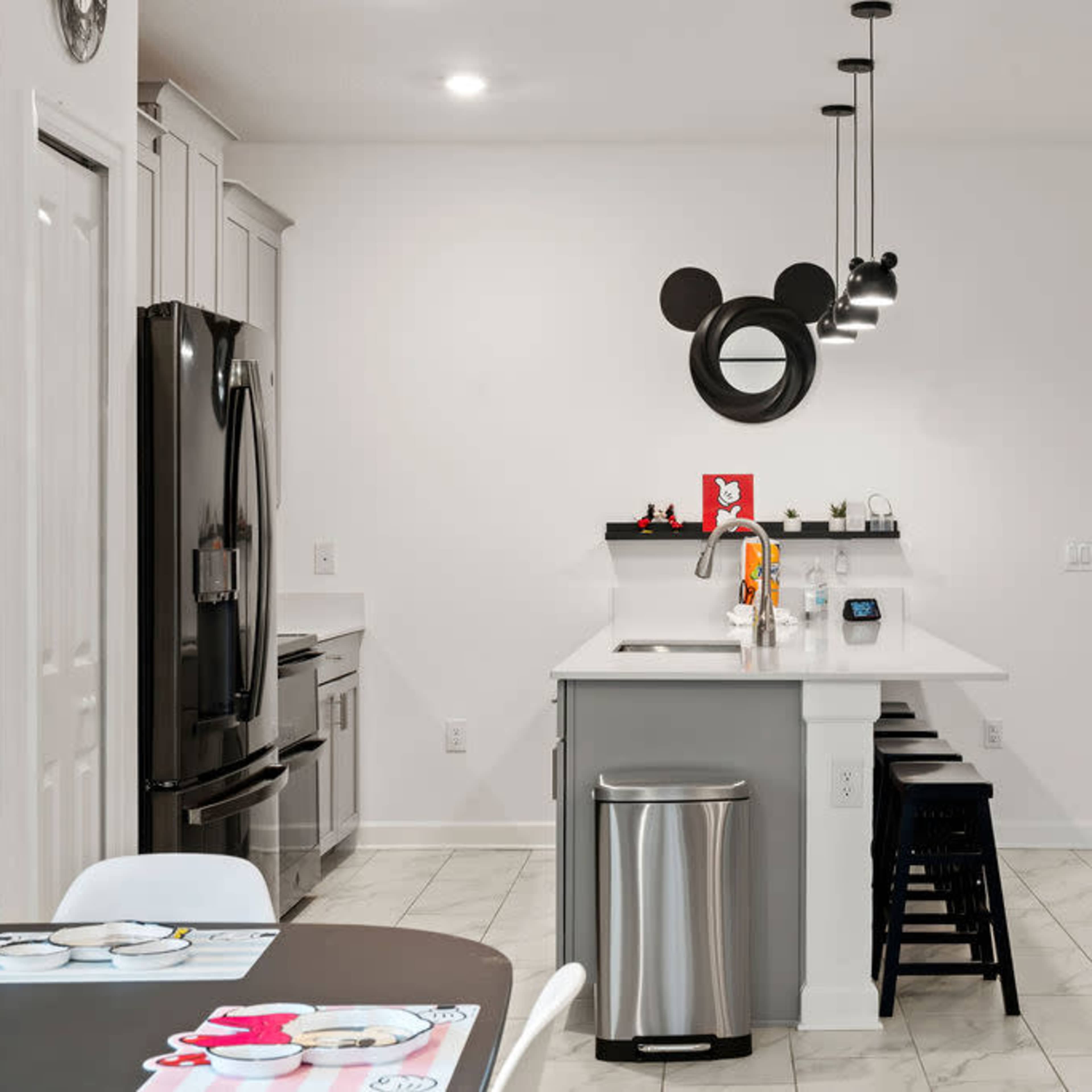A modern kitchen with a Mickey Mouse-themed wall decoration, a central island with bar stools, and sleek appliances.