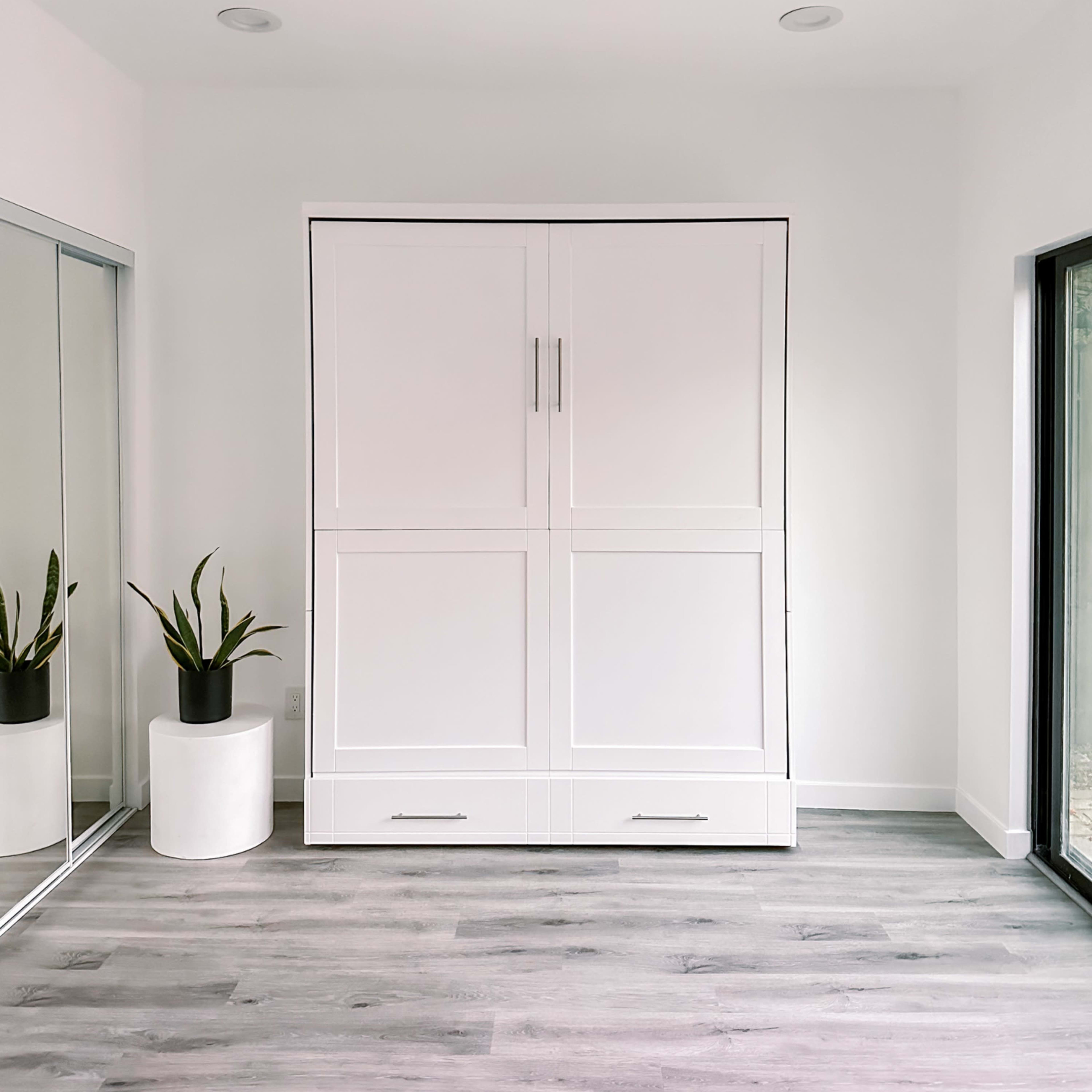 A modern room with a large white cabinet centered on a light-colored floor, alongside a potted plant and a mirrored wardrobe.