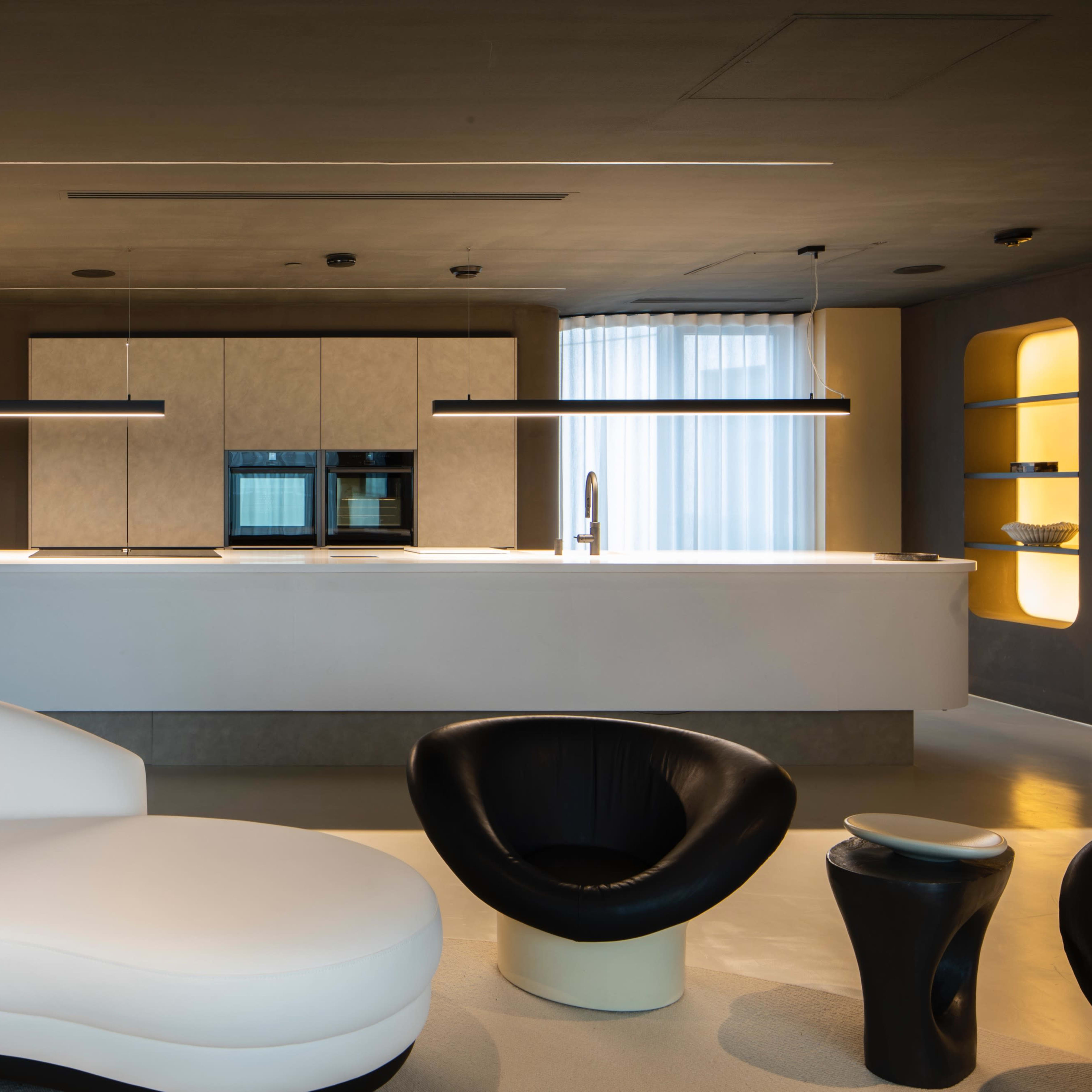 A modern kitchen and living area featuring a curved white sectional sofa, a black chair, and sleek cabinetry with an island countertop.