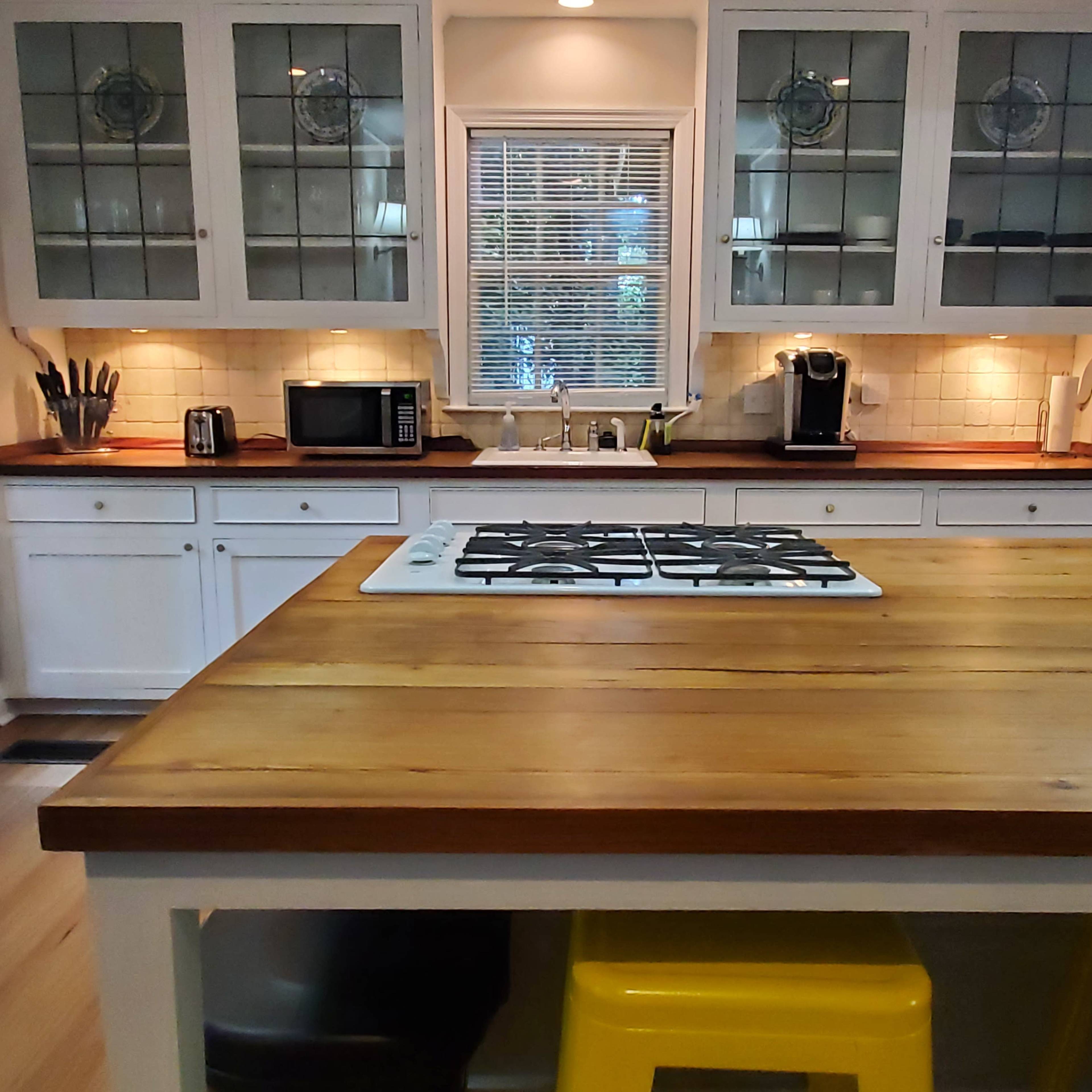 A modern kitchen with white cabinetry, a wooden countertop, and various appliances including a microwave and coffee maker.