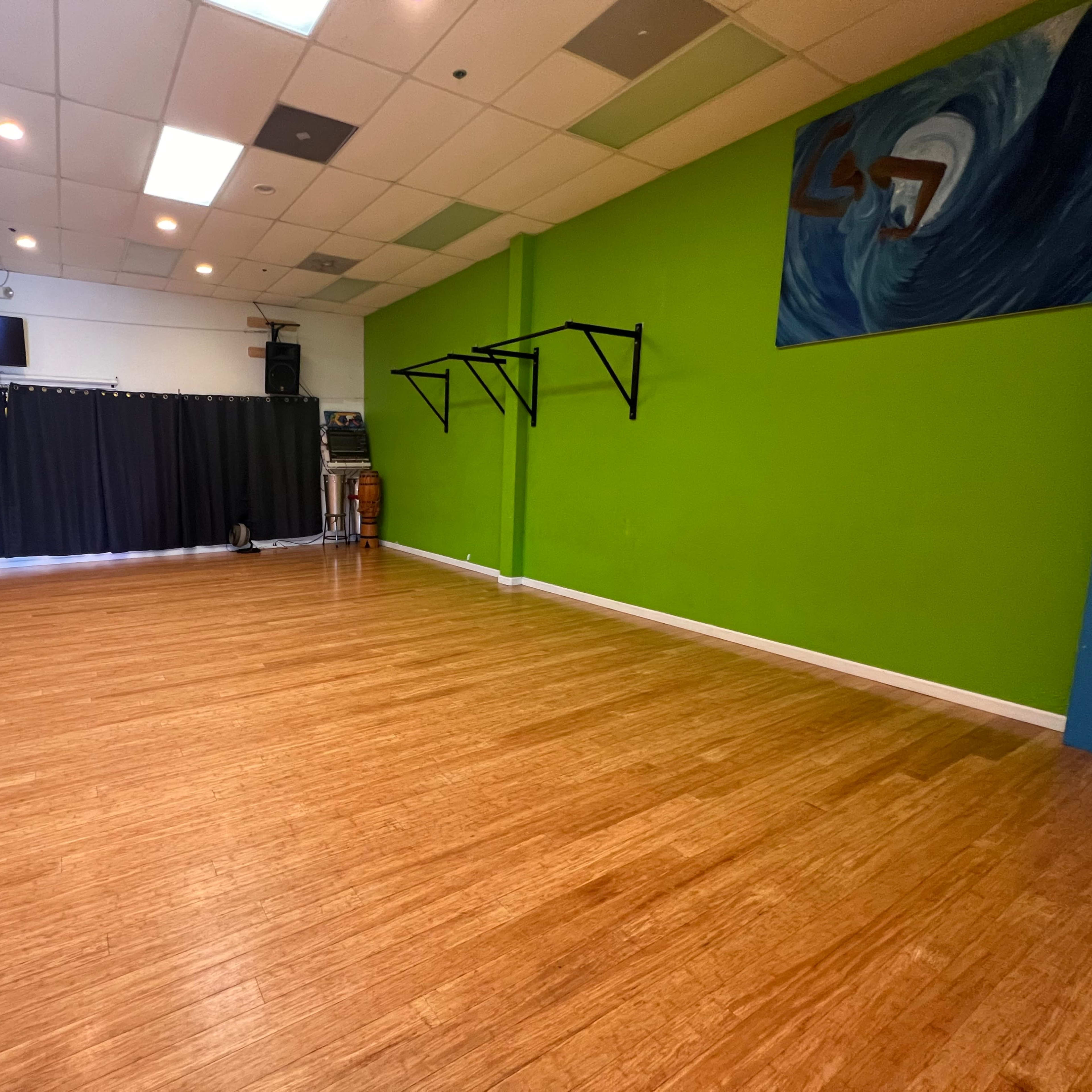 An empty studio space with wooden flooring, green walls, and a black curtain partially drawn at one end.