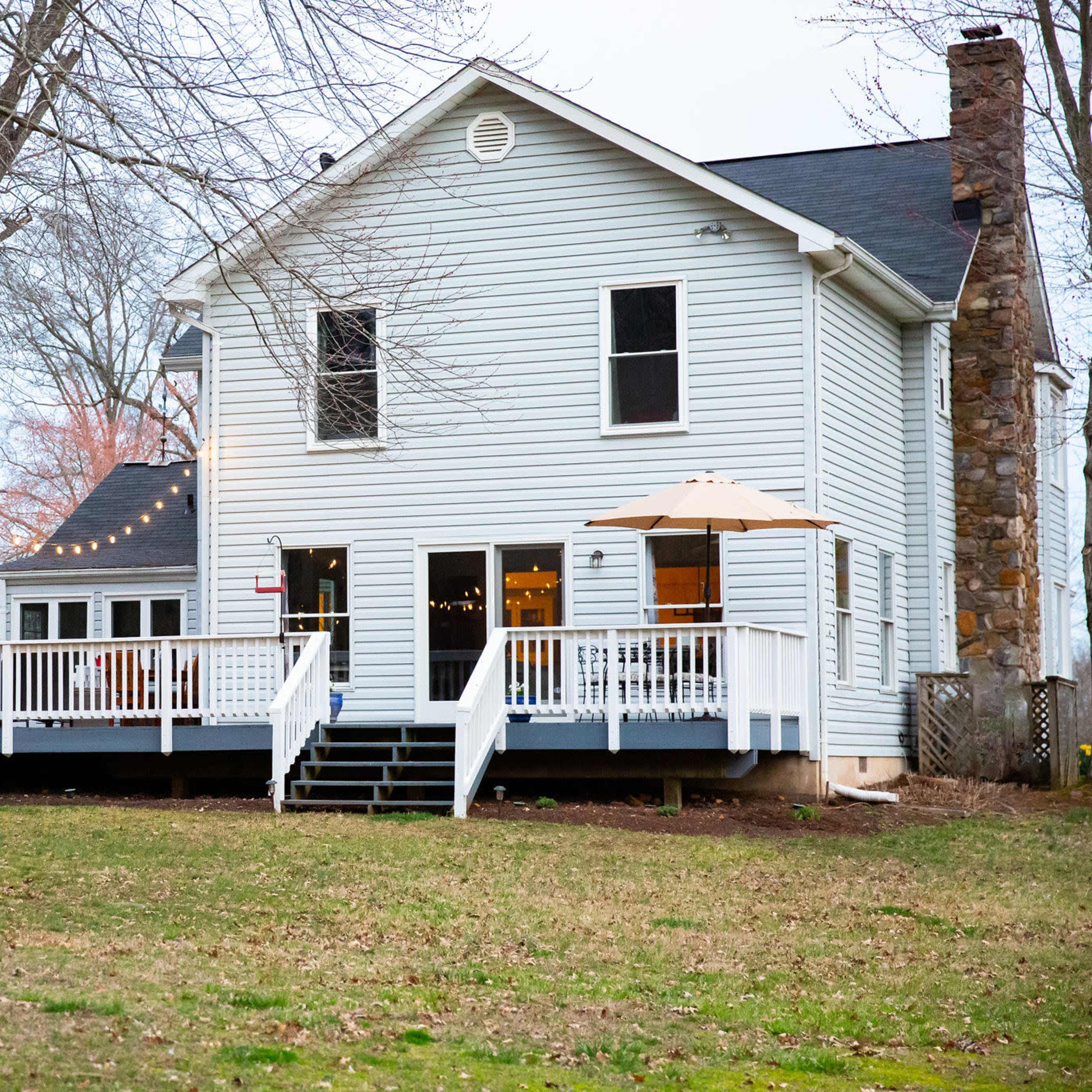 The back of a white two-story house with a deck, surrounded by trees in a grassy yard.