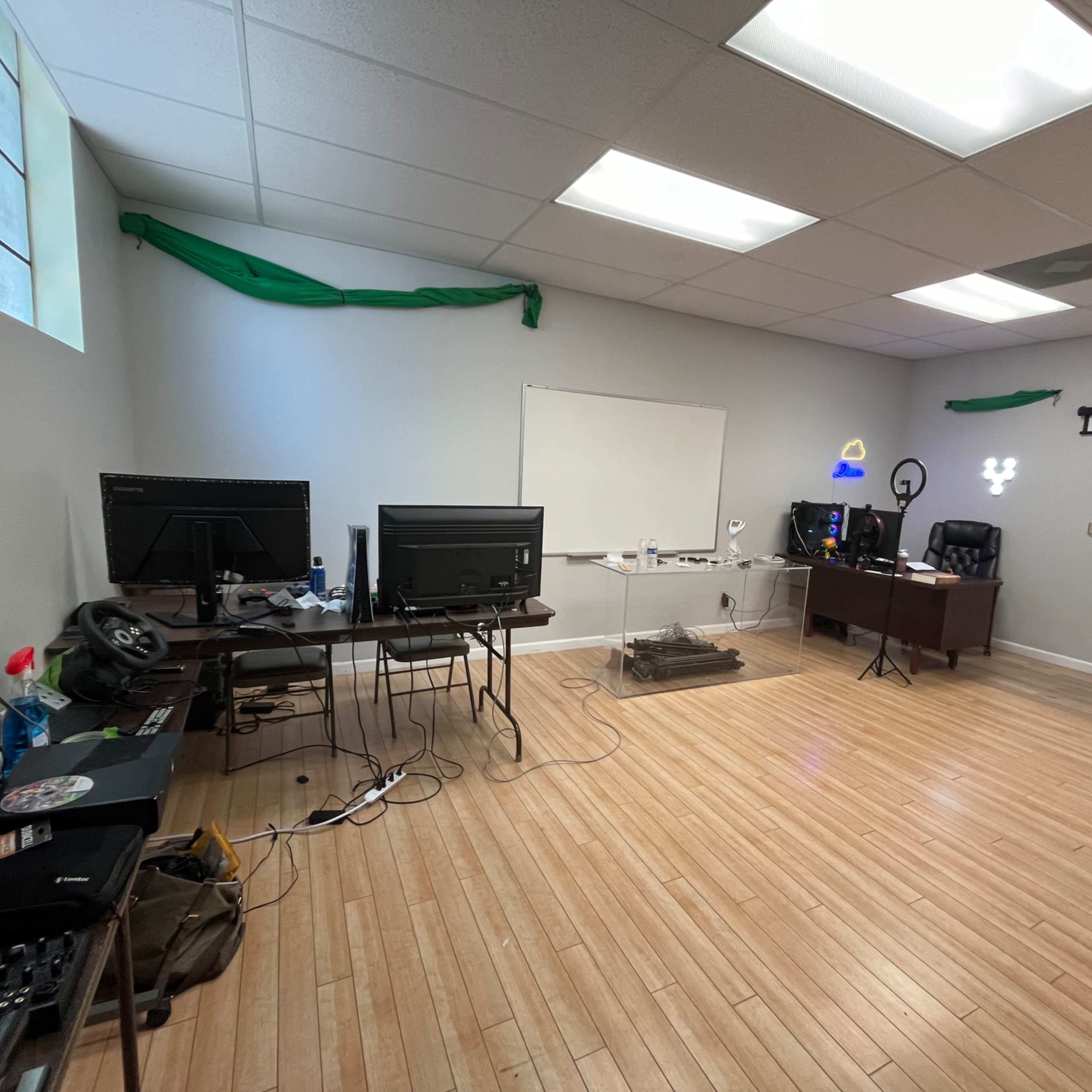An empty office space with two computer desks, a whiteboard, and minimal furniture along with wooden flooring.
