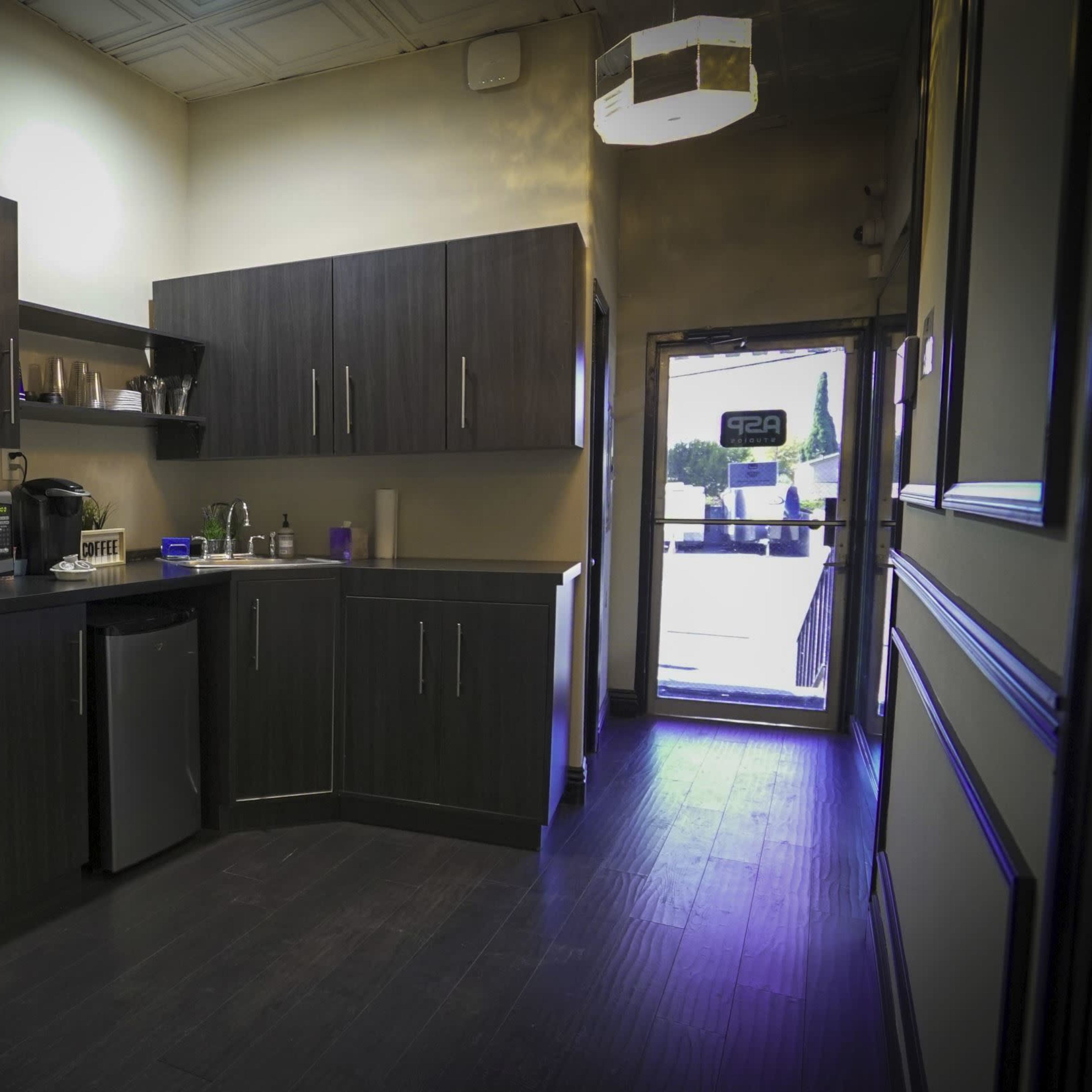A small kitchen area with dark cabinets, a sink, a microwave, a water dispenser, and a doorway leading outside.
