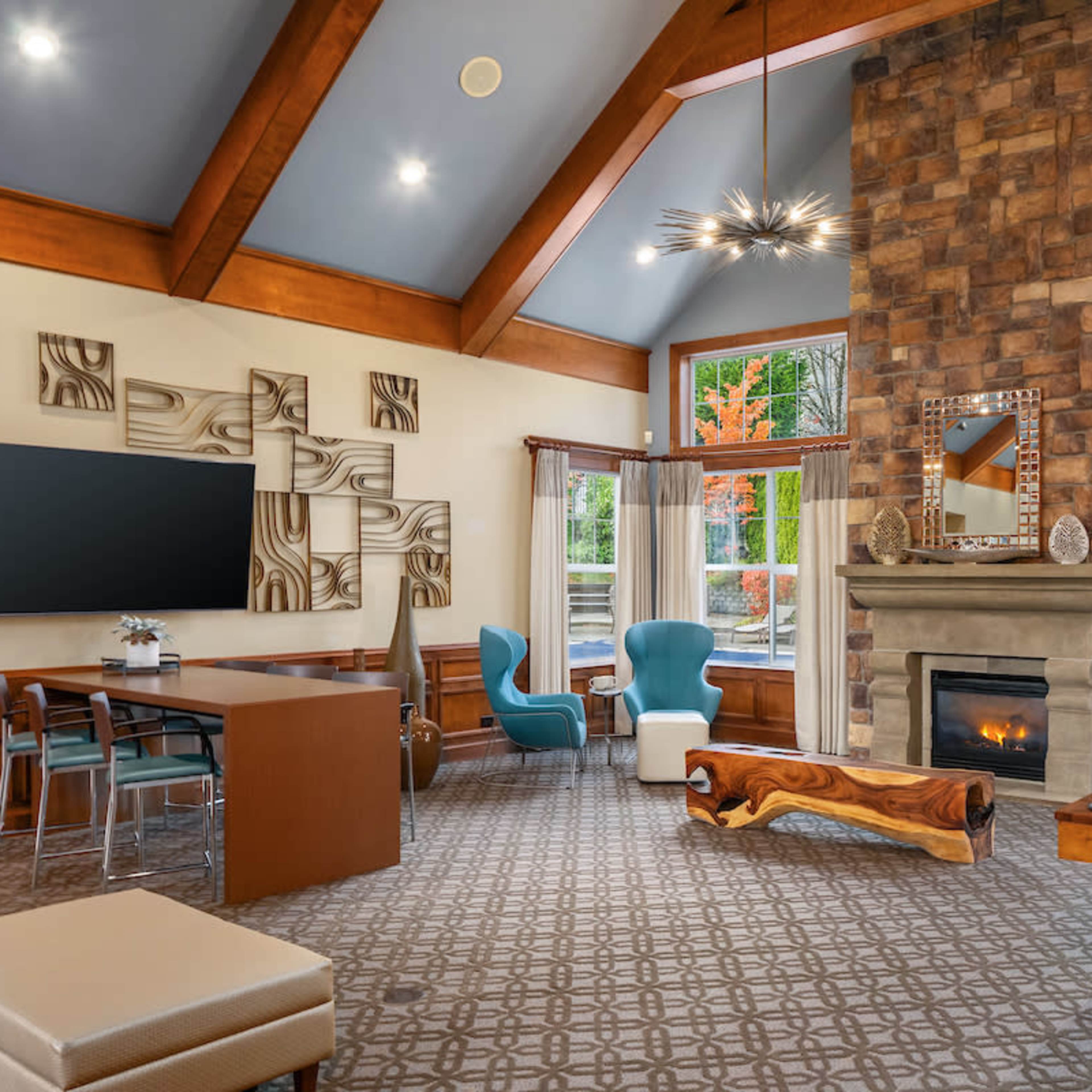 A spacious lounge area featuring a stone fireplace, large windows, modern furniture, and a game table.